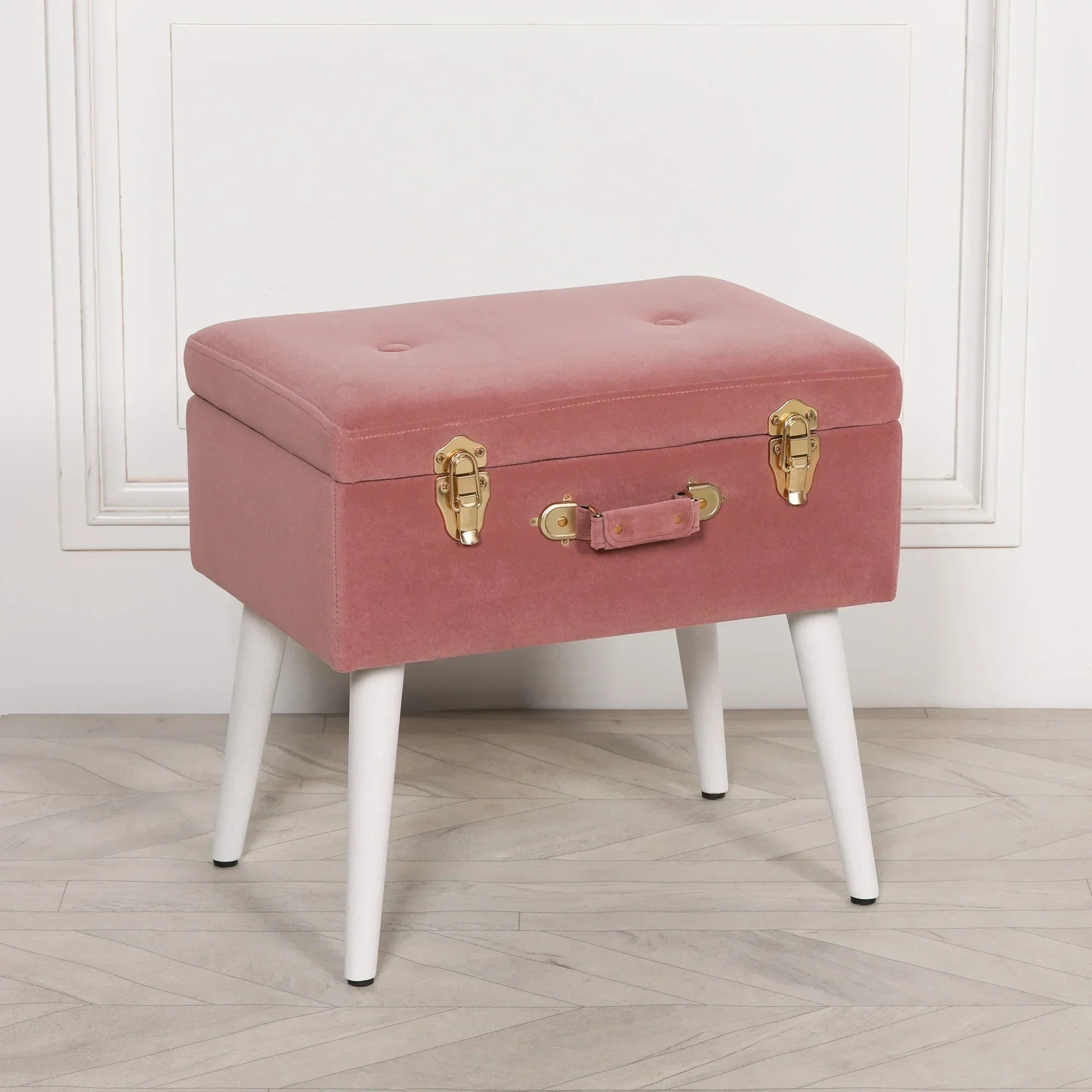 Pink velvet storage bench with gold clasps and white tapered legs on wooden floor