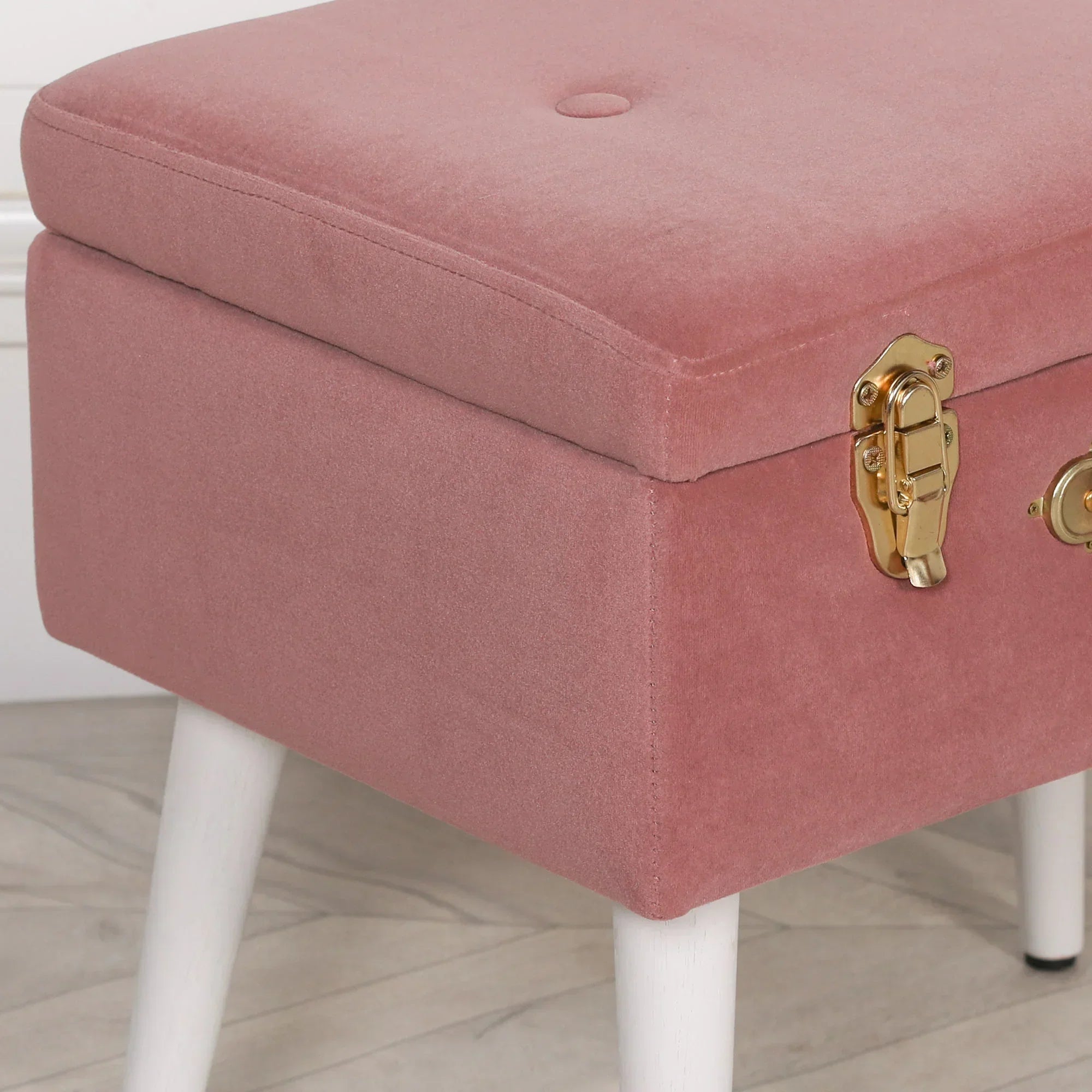 Pink velvet storage ottoman bench with gold latch and white wooden legs on wood floor