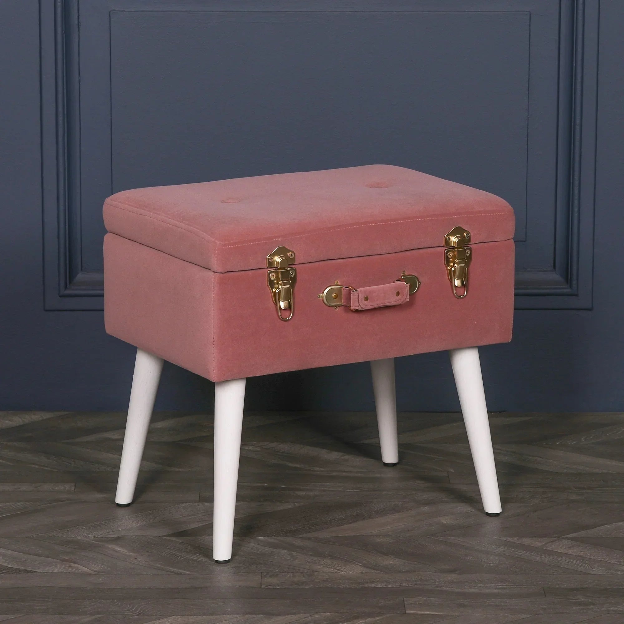 Pink velvet storage stool with gold clasps and white tapered legs on wood floor