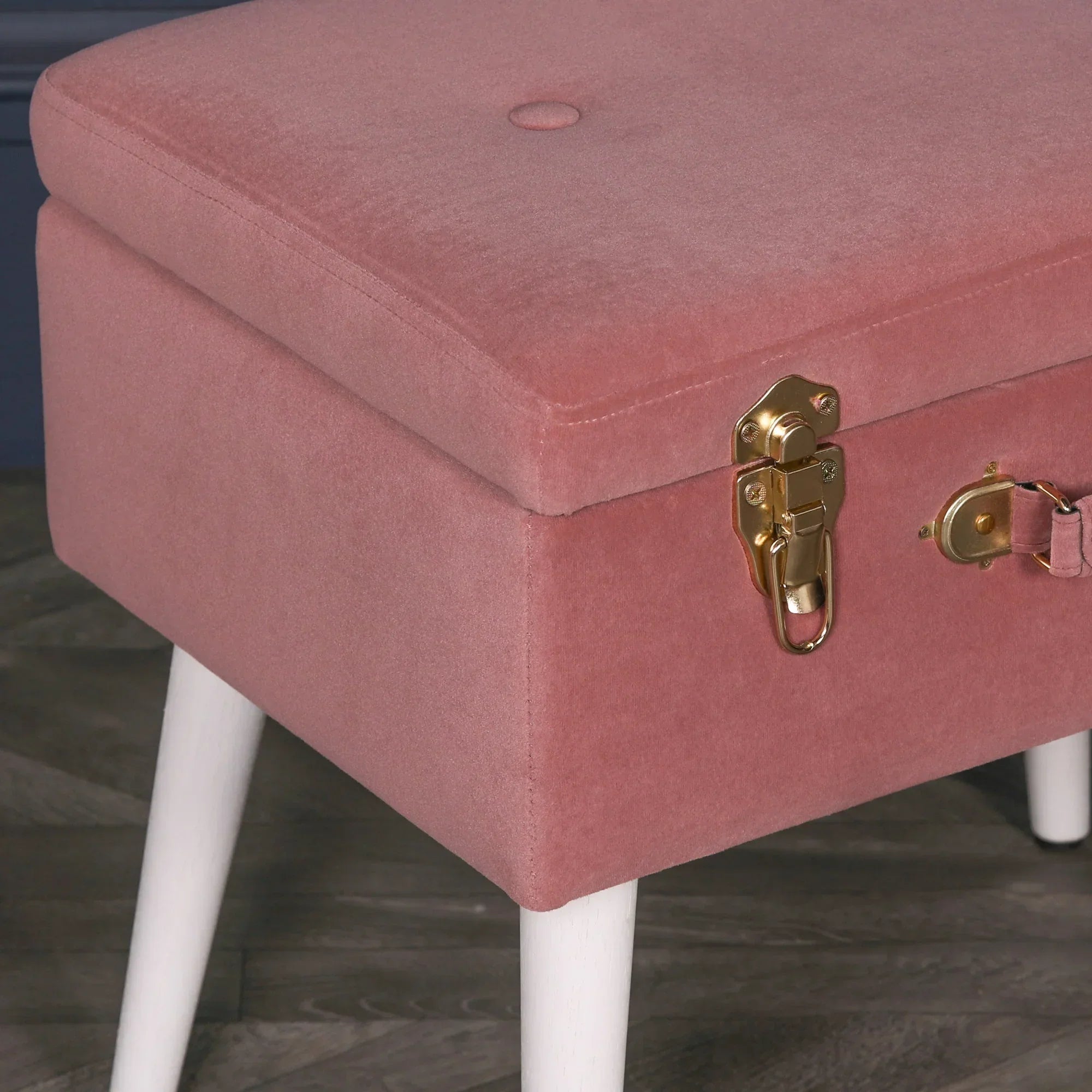 Pink velvet storage bench with gold latch detail and white wooden legs on wood floor