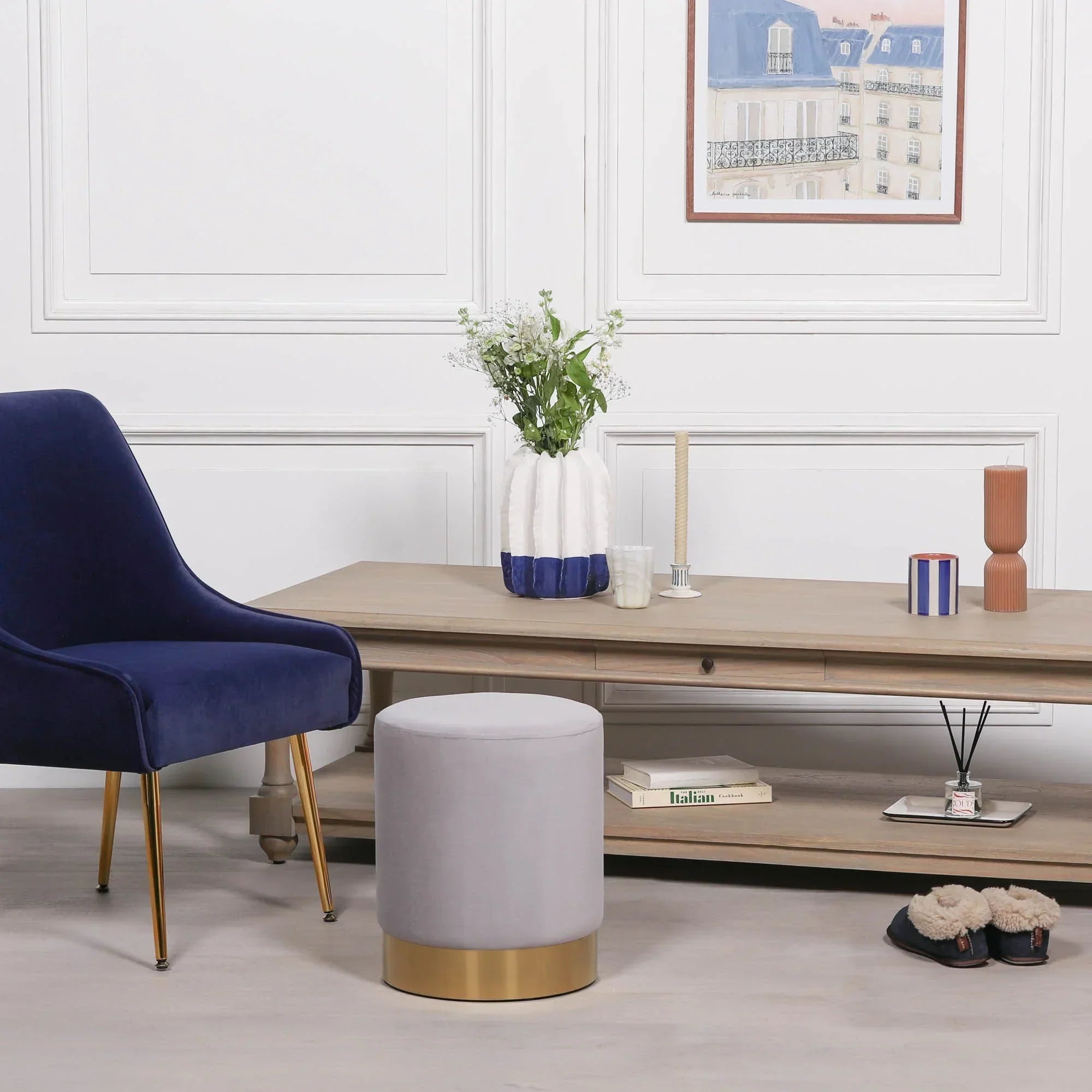 Grey velvet stool with gold base beside navy accent chair and wooden coffee table in living room