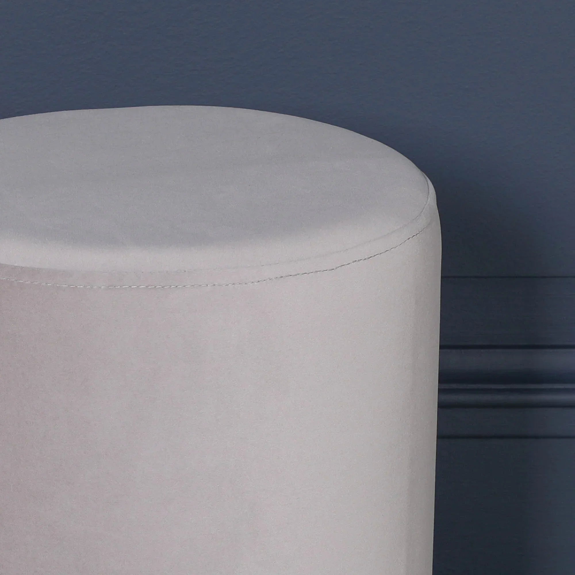 Light grey velvet round stool against dark blue wall