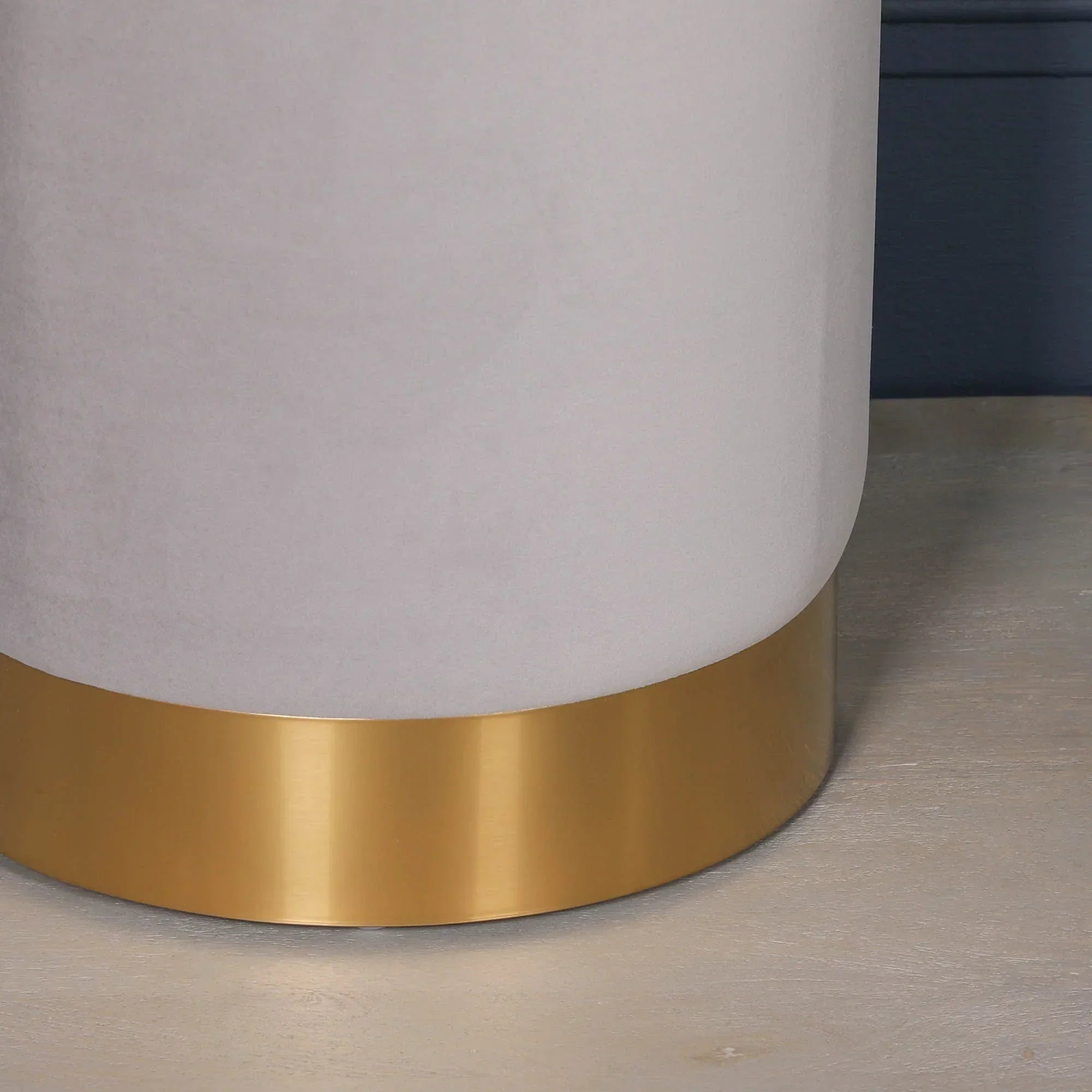 Close-up of round ottoman with light grey upholstery and gold metal base on wood floor