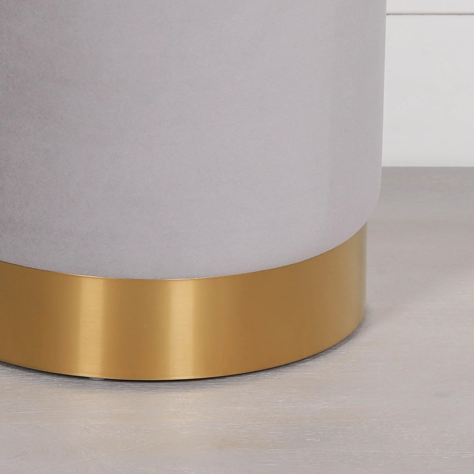Close-up of furniture base with brushed gold metal trim and light grey upholstery