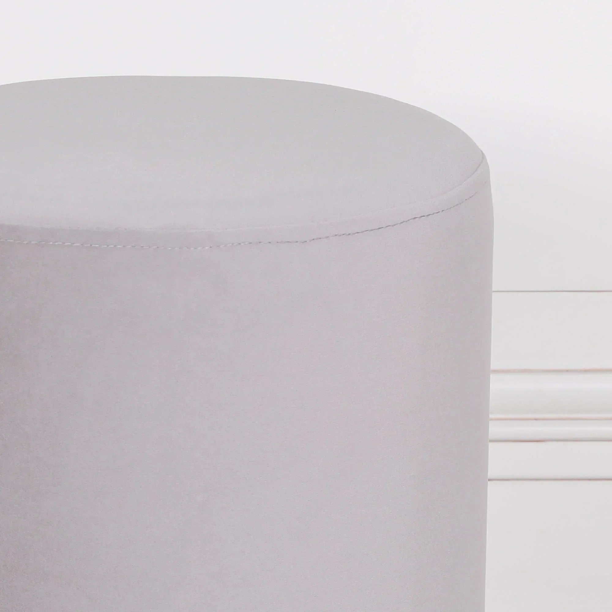 Light grey velvet ottoman stool with round shape placed against white wall