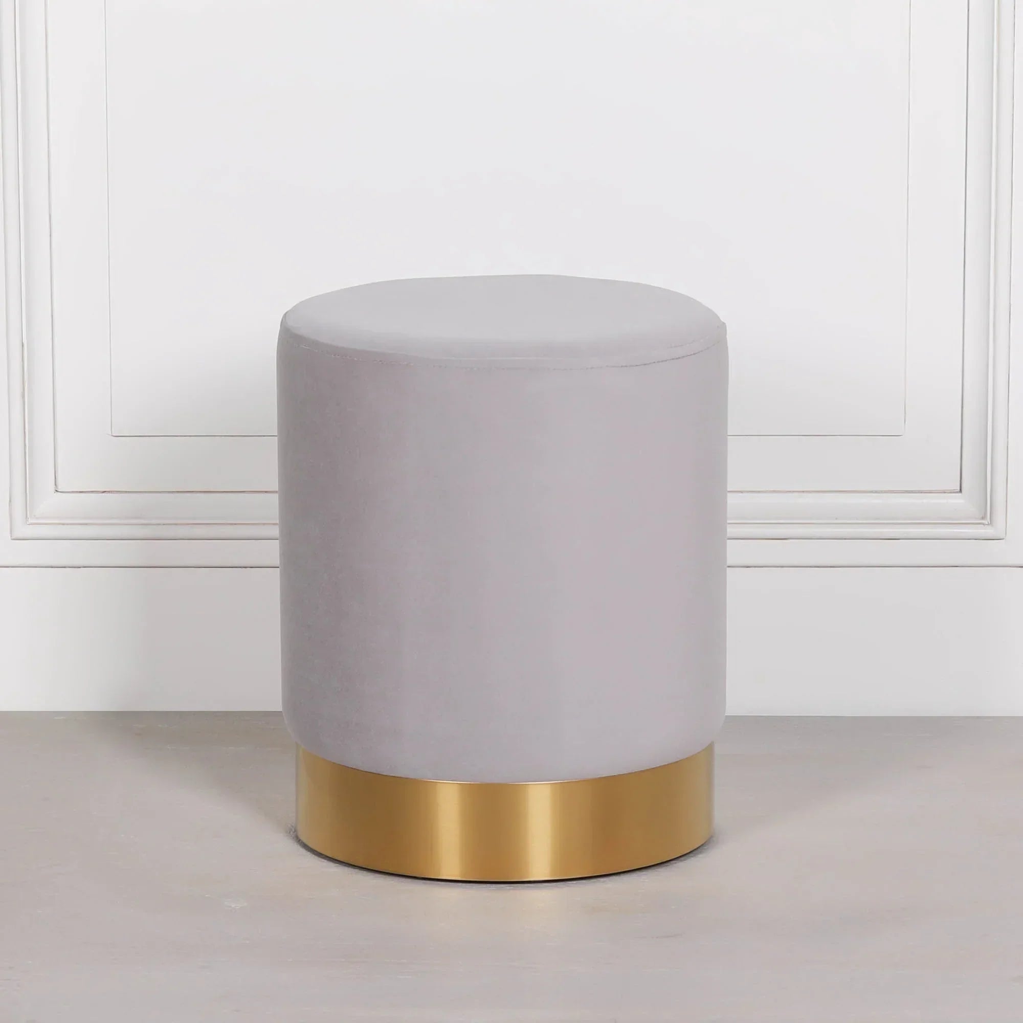 Grey velvet stool with gold base on light floor against white paneled wall