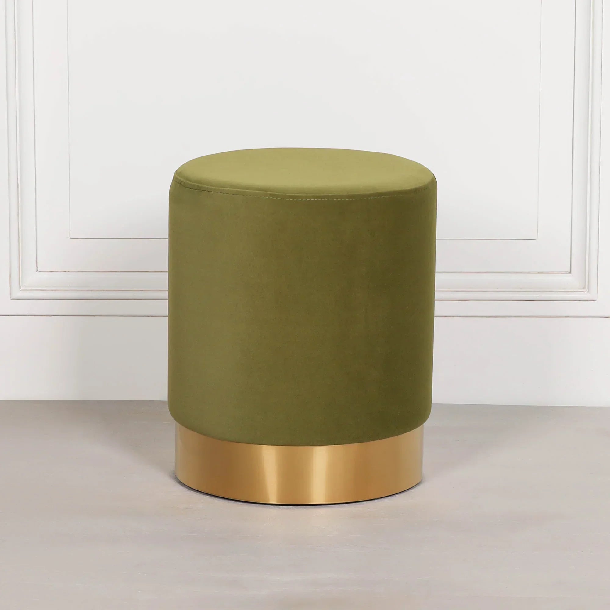 Green velvet ottoman stool with gold metal base against white wall