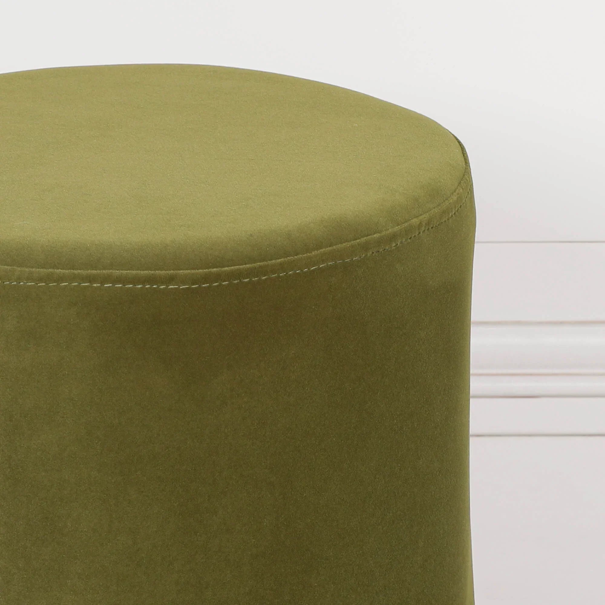 Green velvet ottoman close-up showing round seat and soft fabric texture
