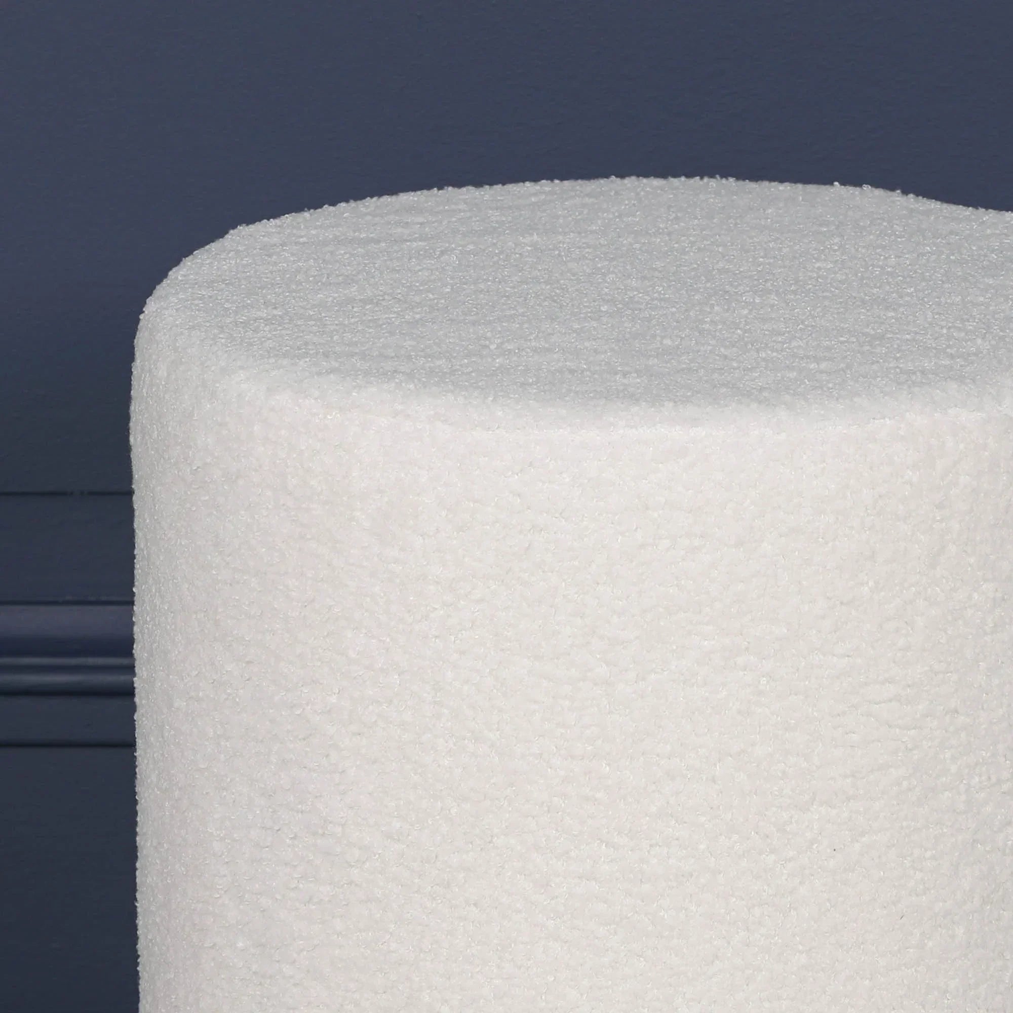 Close-up of white boucle ottoman against dark blue wall