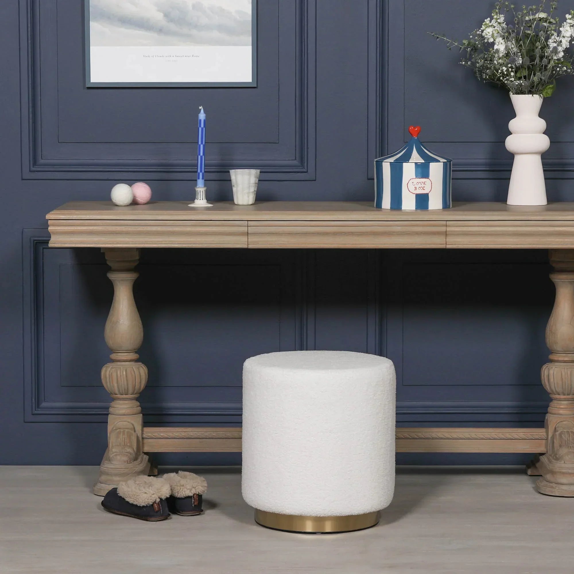 White boucle footstool with gold base in front of wooden console table in a modern room