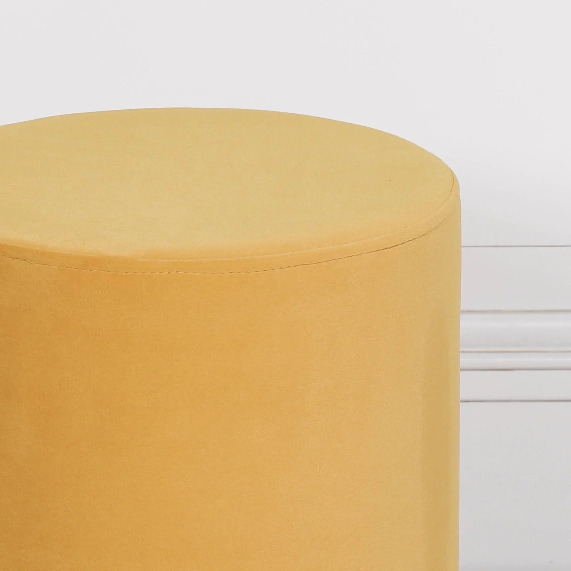 Mustard yellow velvet round ottoman against white wall