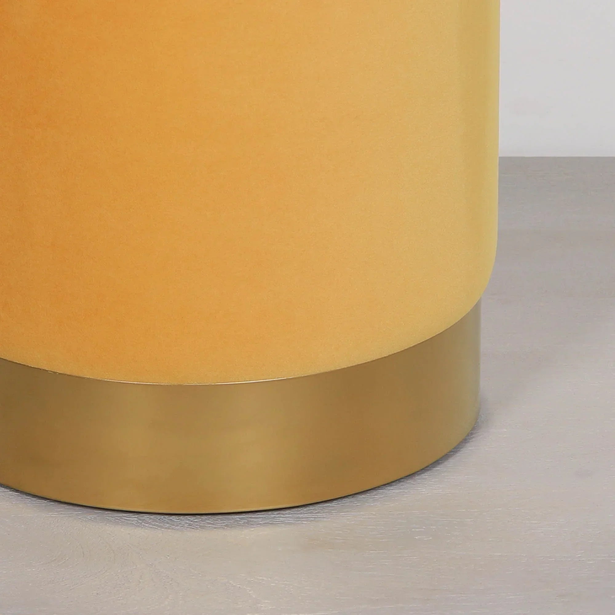 Mustard yellow velvet ottoman with gold metal base on light wood floor