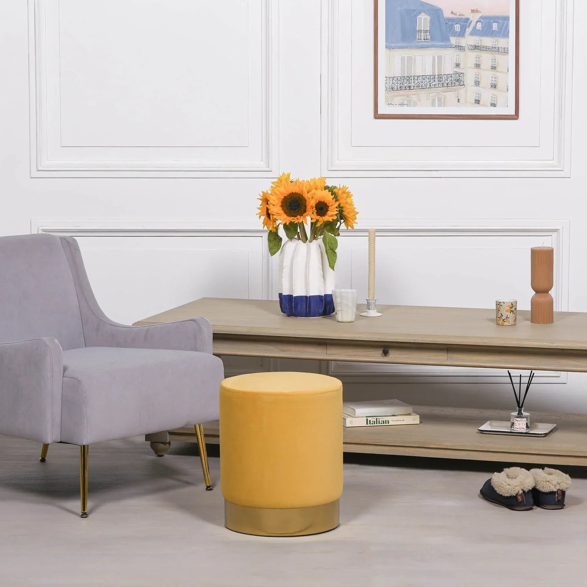 Yellow velvet footstool with gold base beside grey armchair in modern living room setting