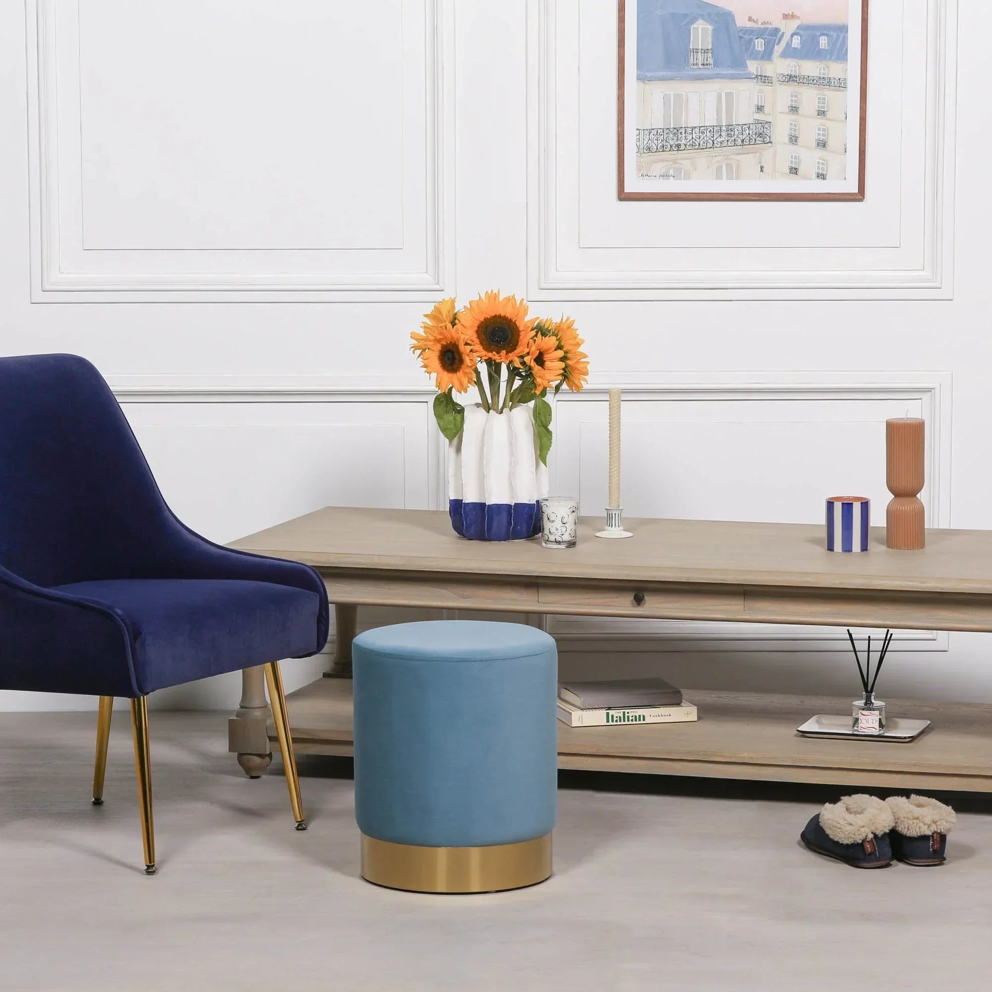 Blue velvet accent chair and round ottoman with gold base beside wooden coffee table in living room