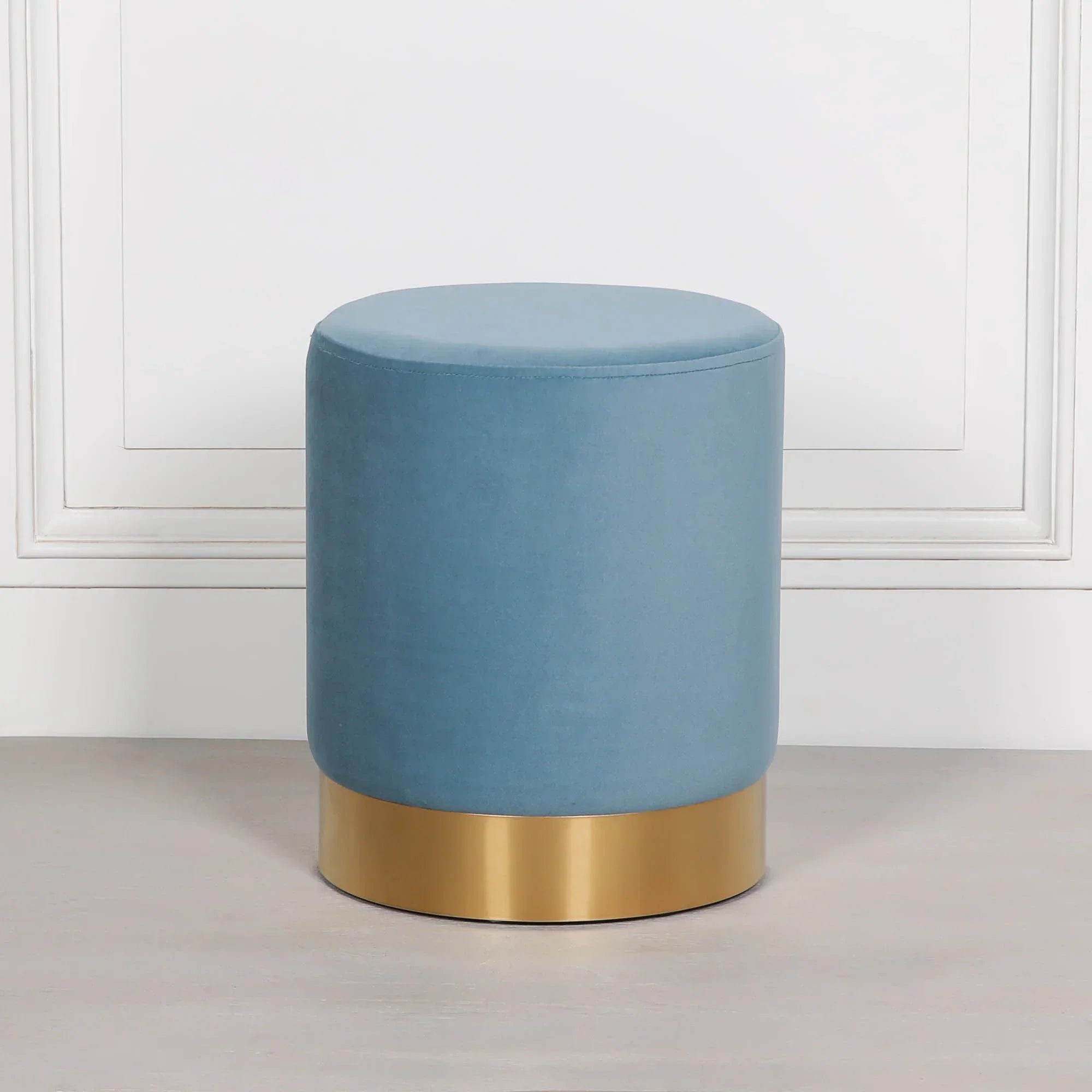 Blue velvet stool with gold metal base against white panel wall