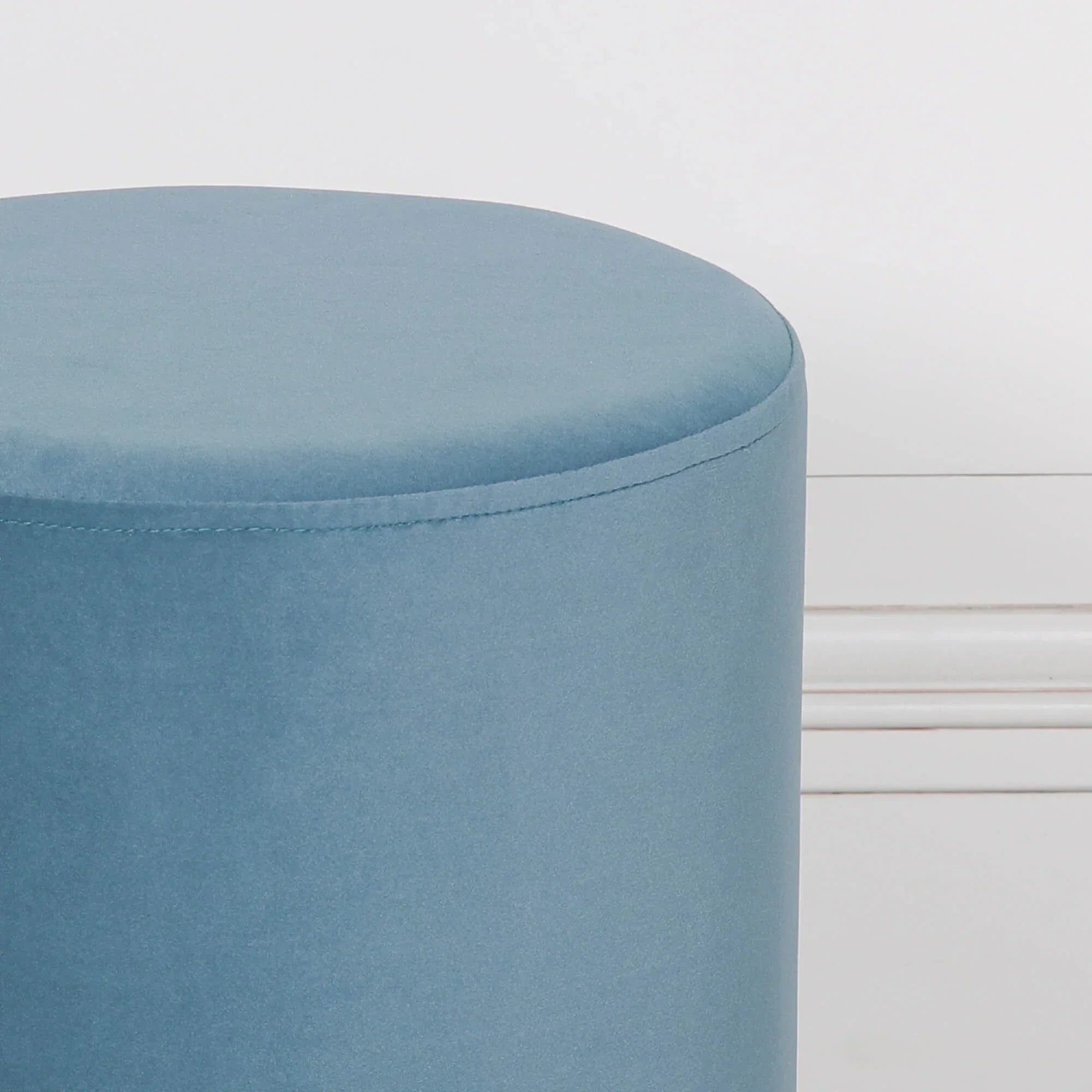 Blue velvet round ottoman against white wall close-up