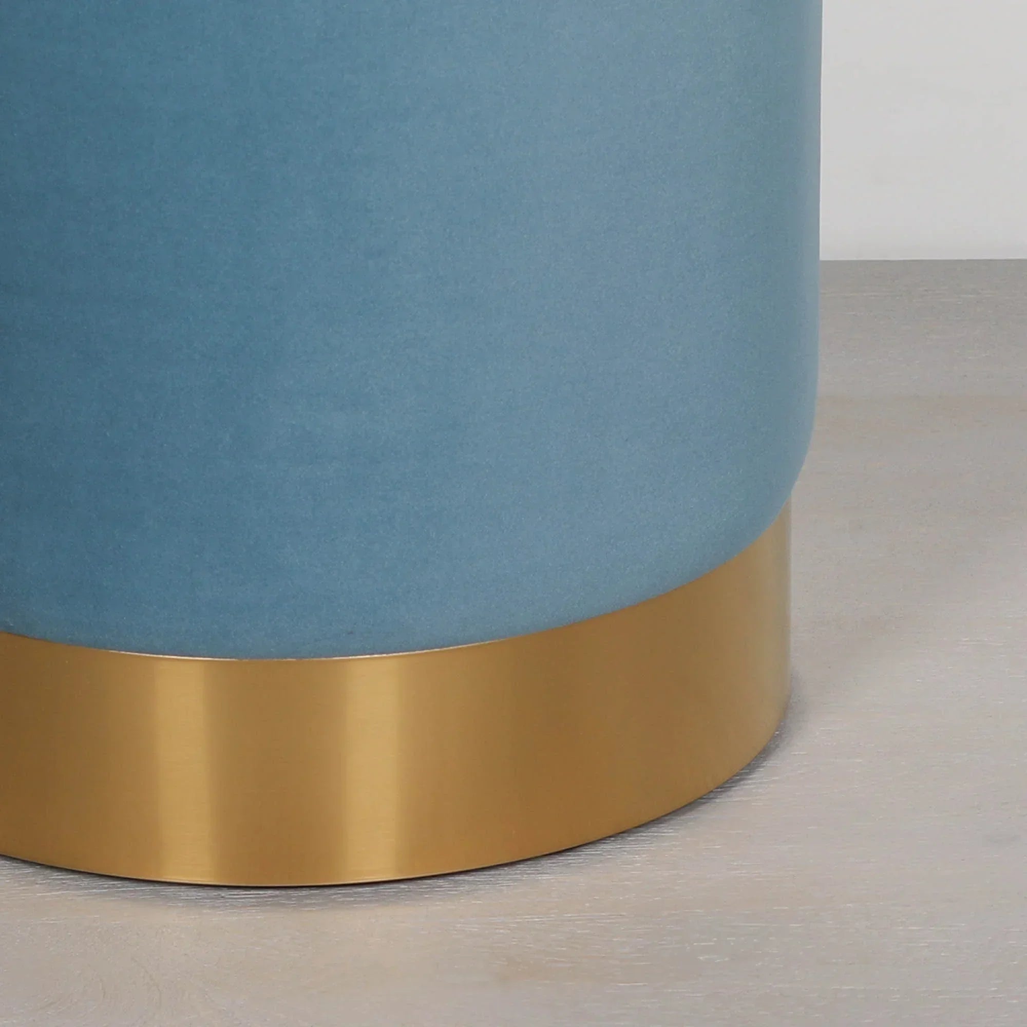 Blue velvet stool with gold metal base on light wood floor, side angle view