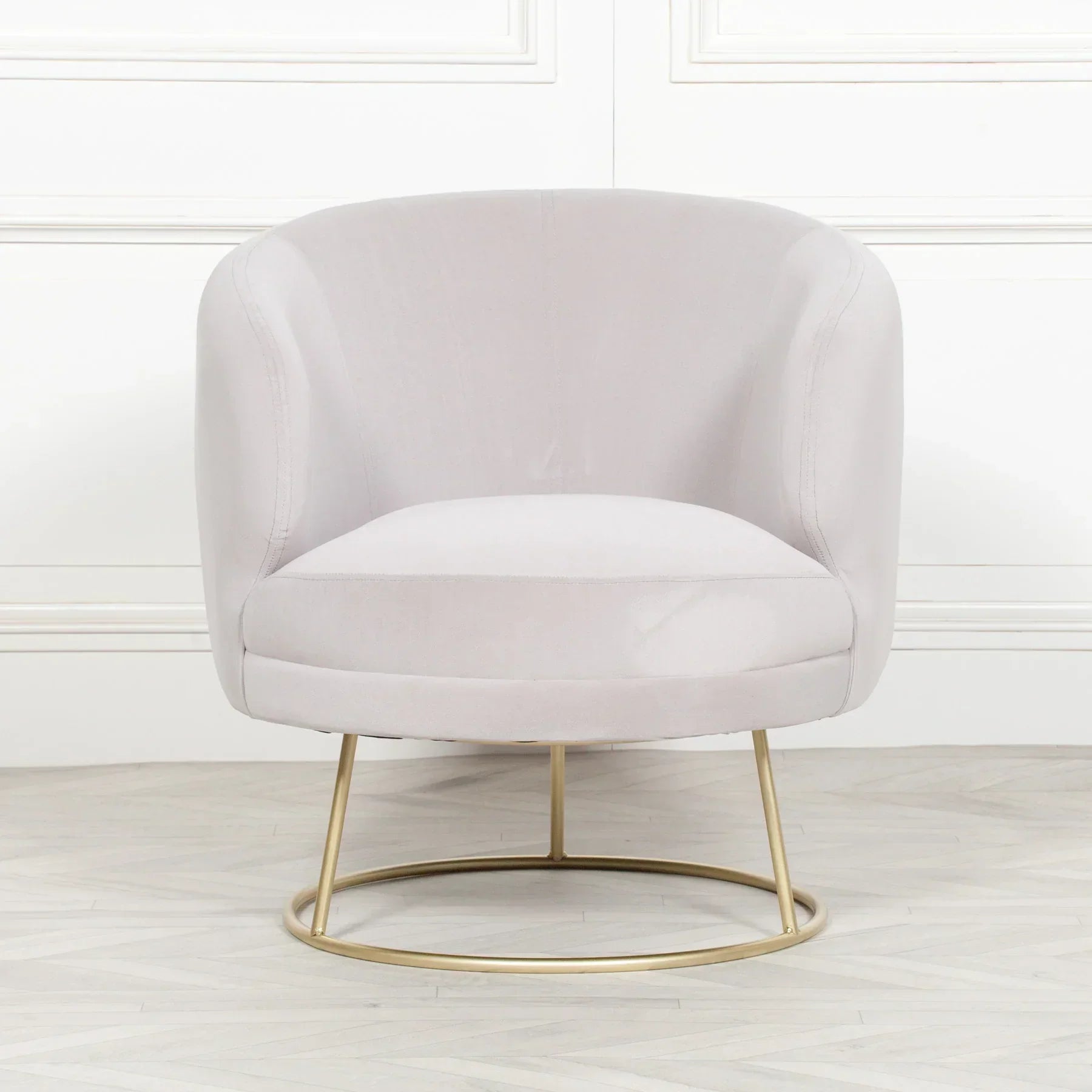 Light grey velvet accent chair with gold metal base on wooden floor