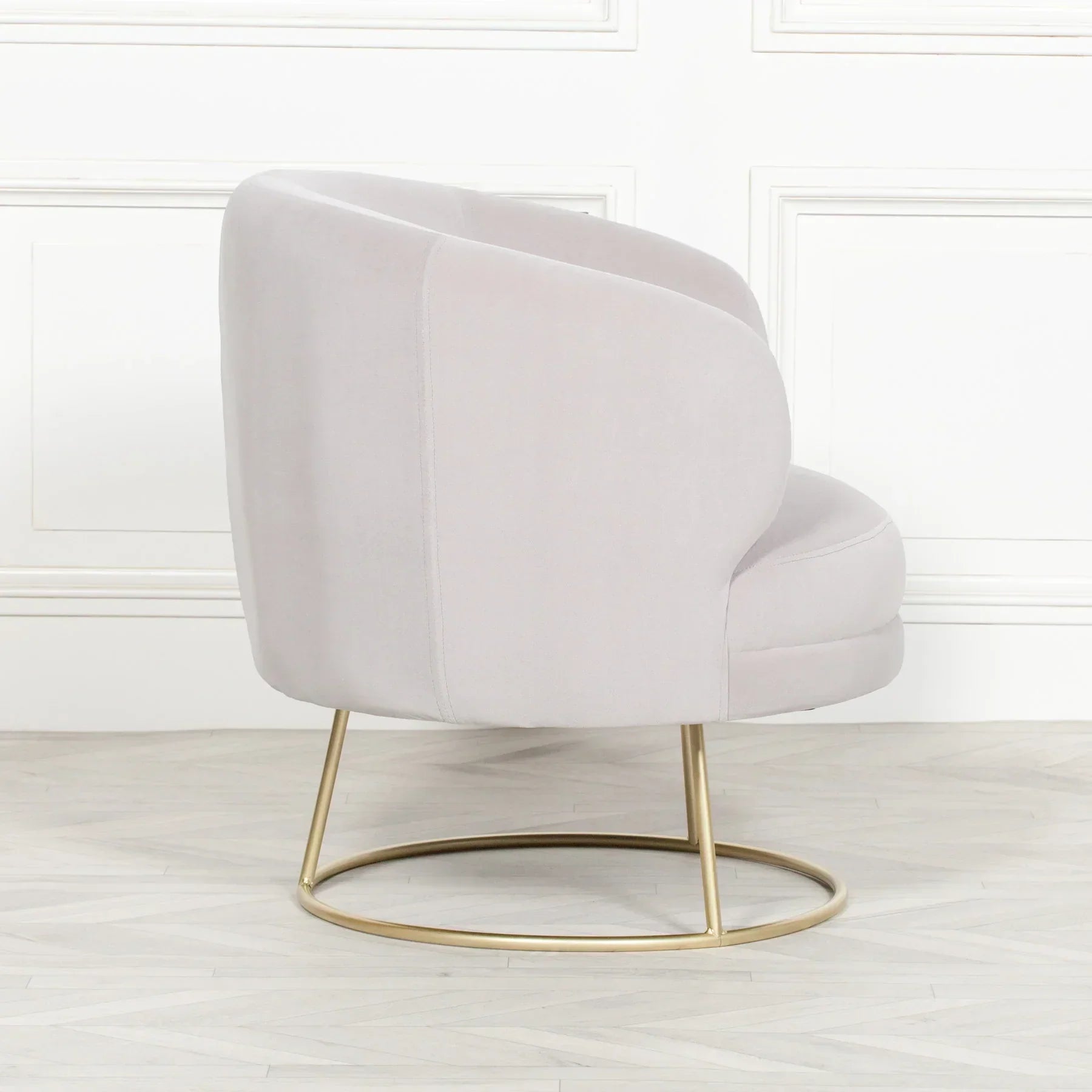 Light grey velvet accent chair with curved back and gold metal base on wood floor