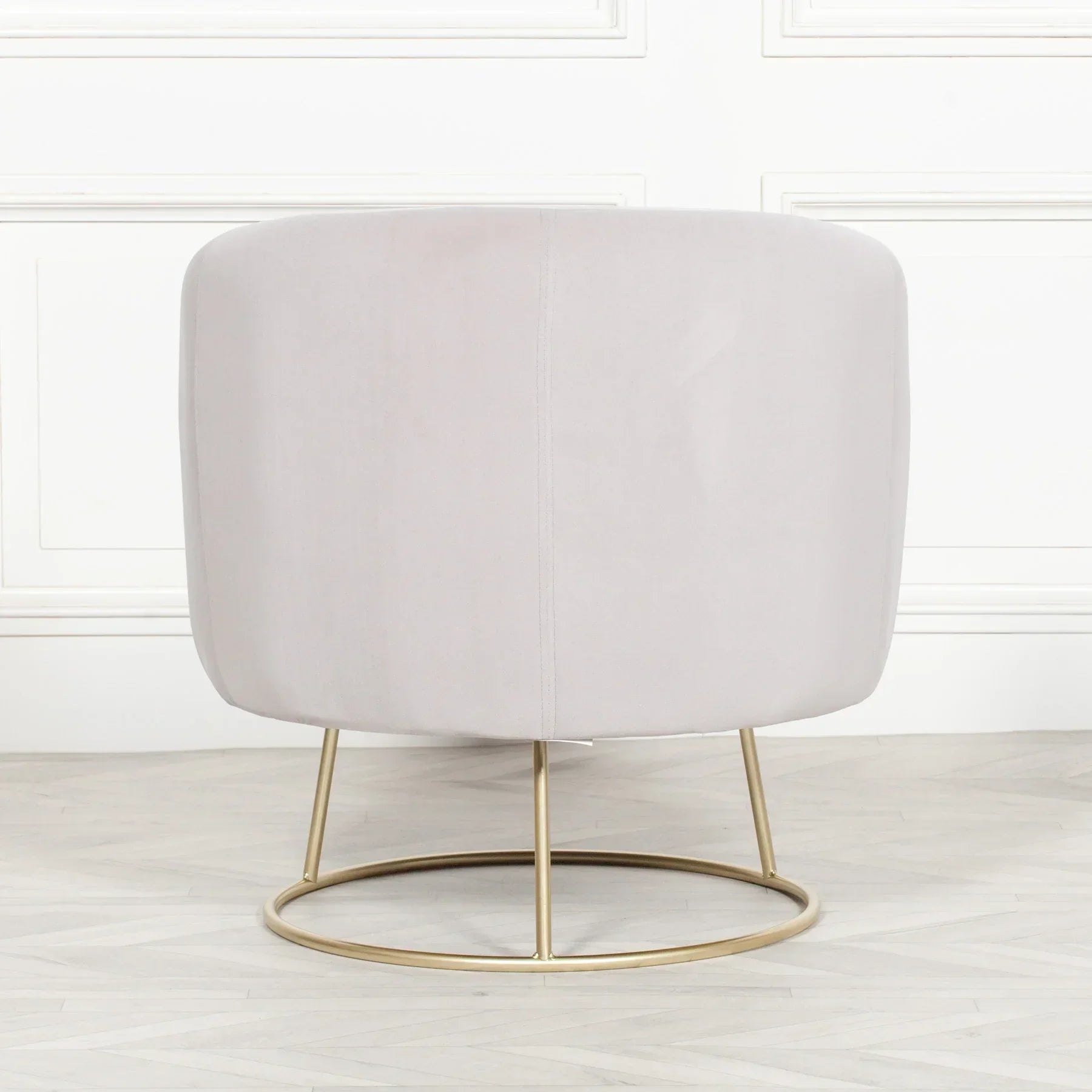 Back view of a velvet accent chair with gold metal base on light wood floor