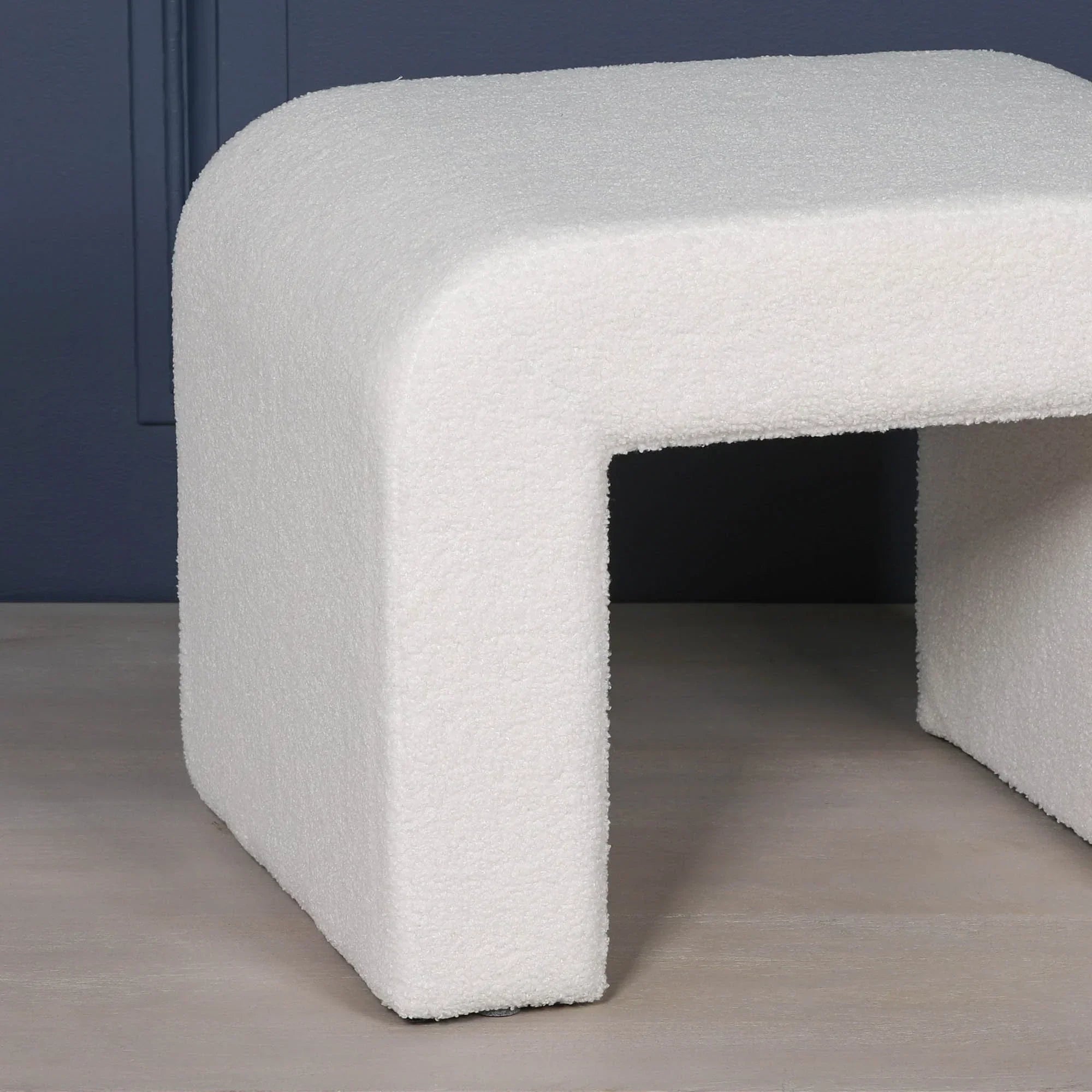 White boucle fabric stool with modern curved edges against a dark blue wall