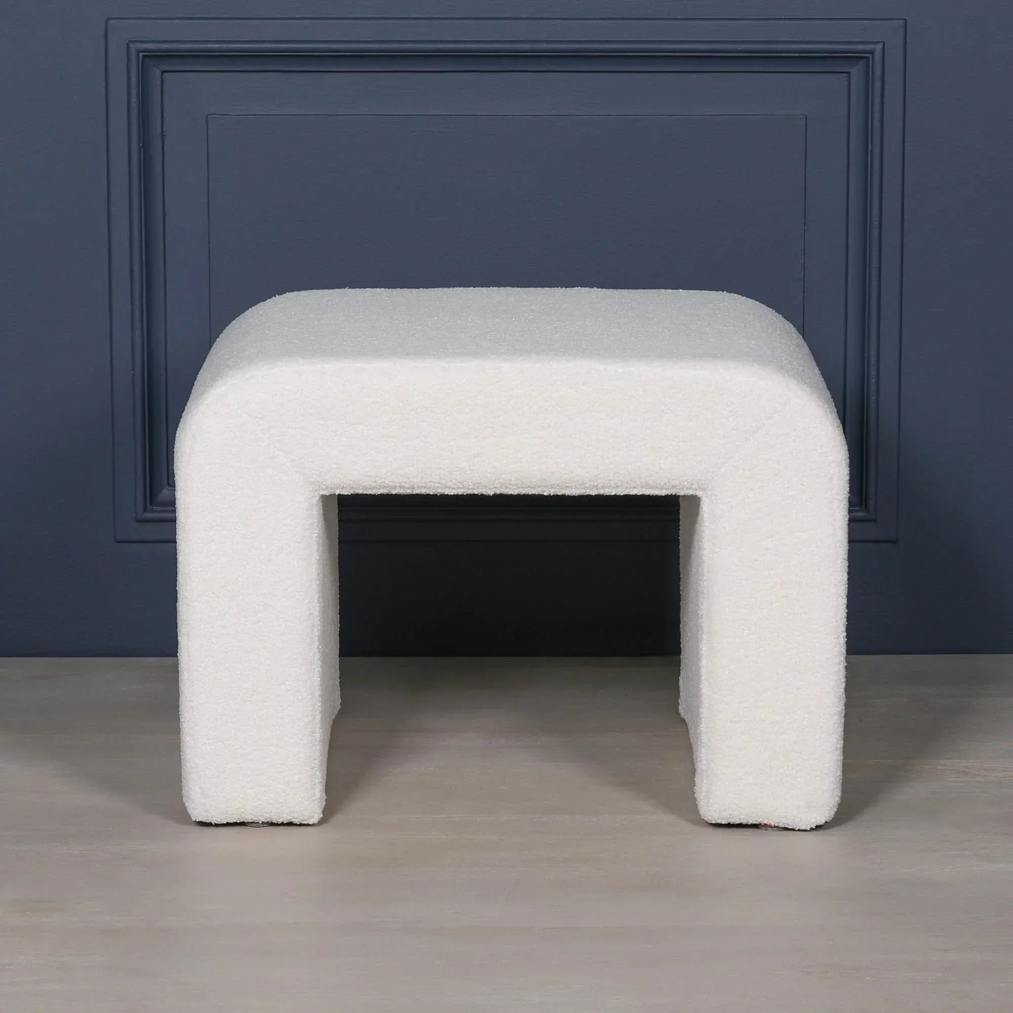Curved white boucle upholstered bench with modern legs in front of navy wall panel