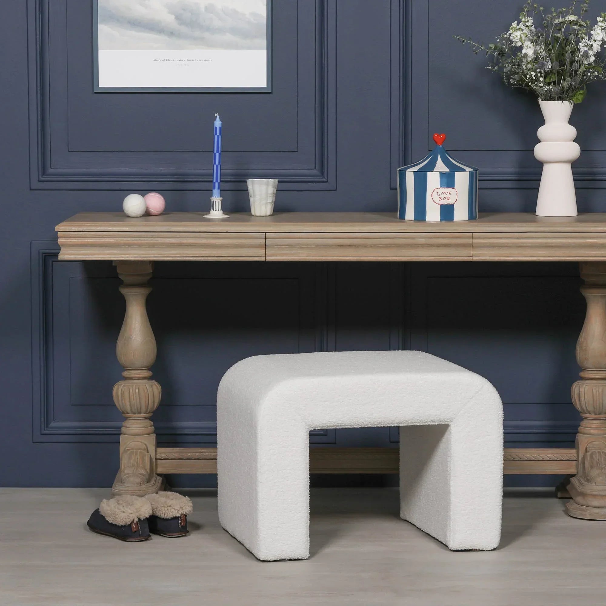 White boucle bench stool in front of wooden console table with decorative accents