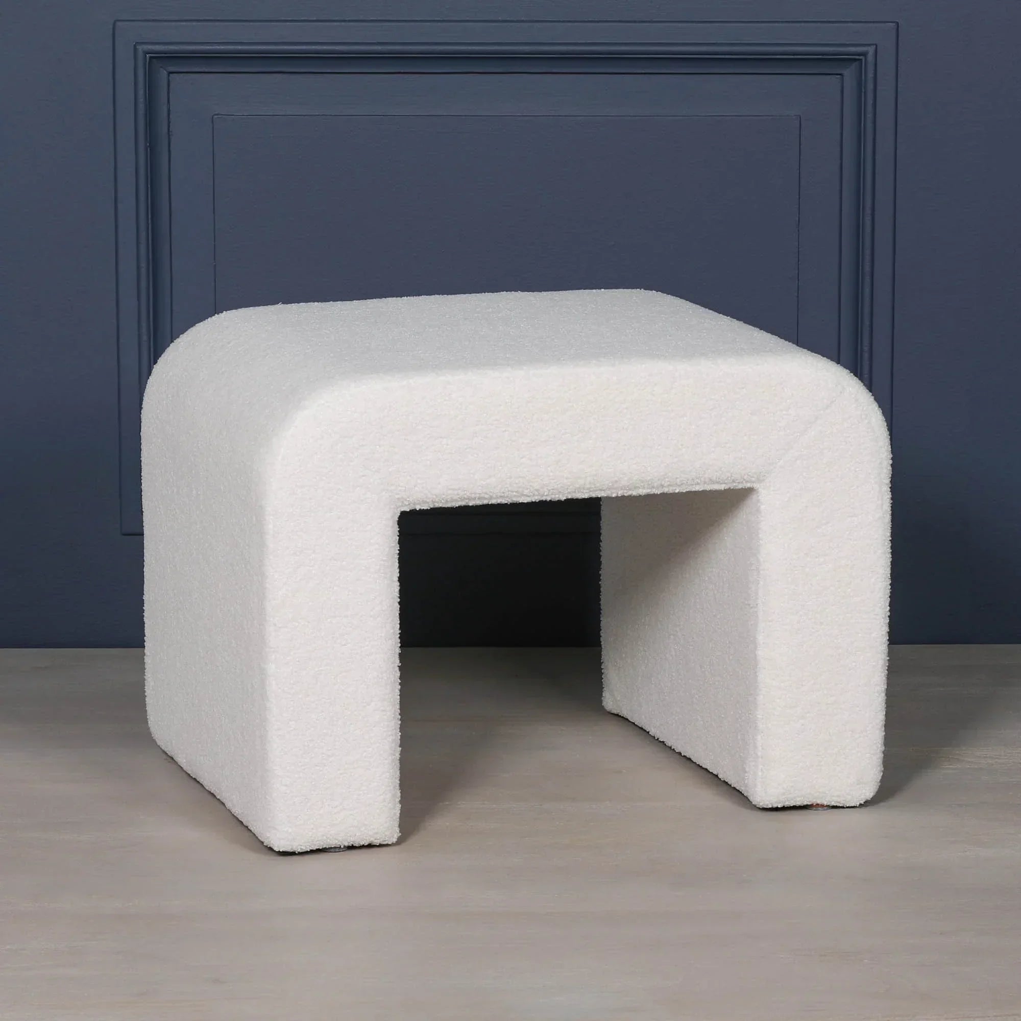 Modern white boucle ottoman bench with curved edges against blue wall