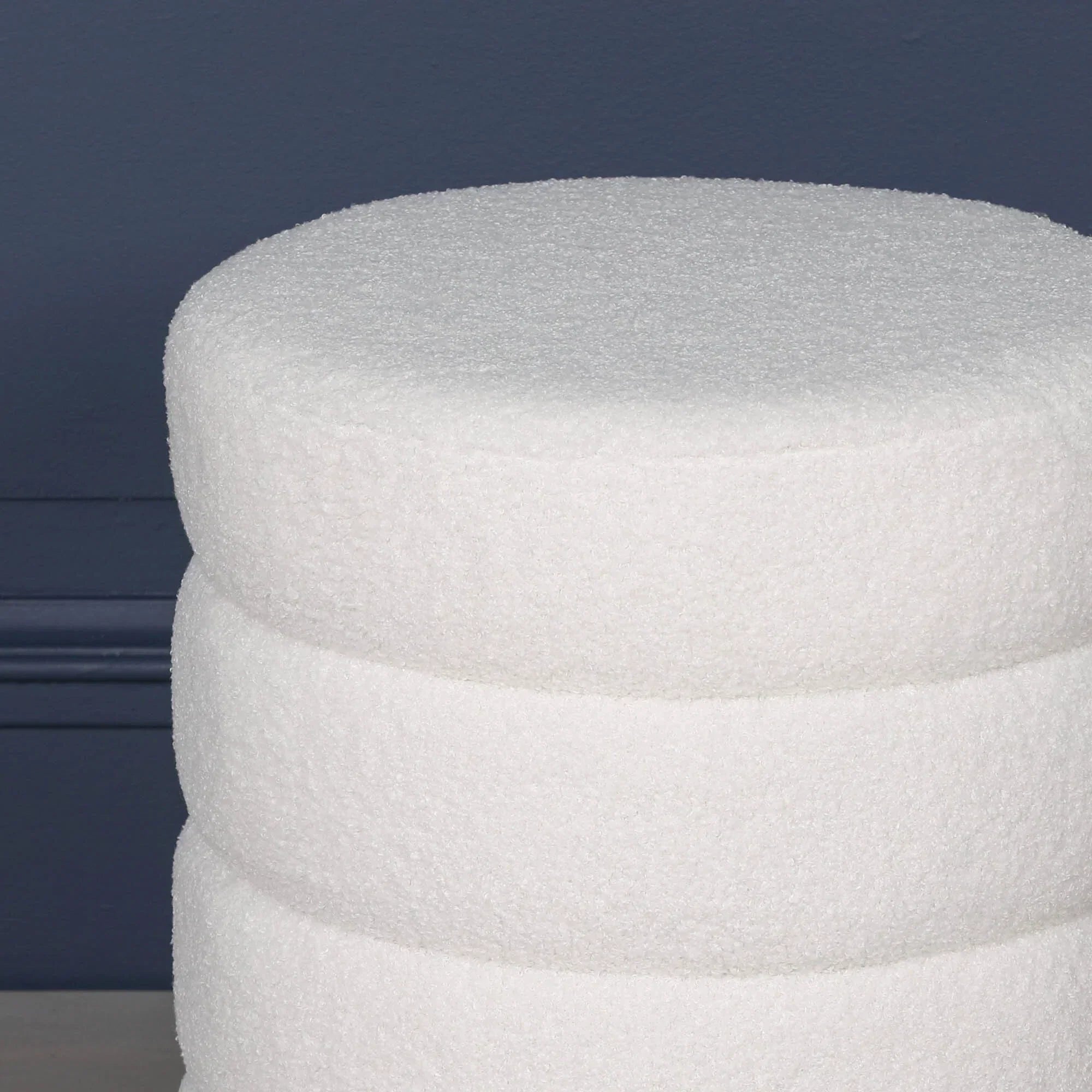 White boucle ottoman stool against dark blue wall