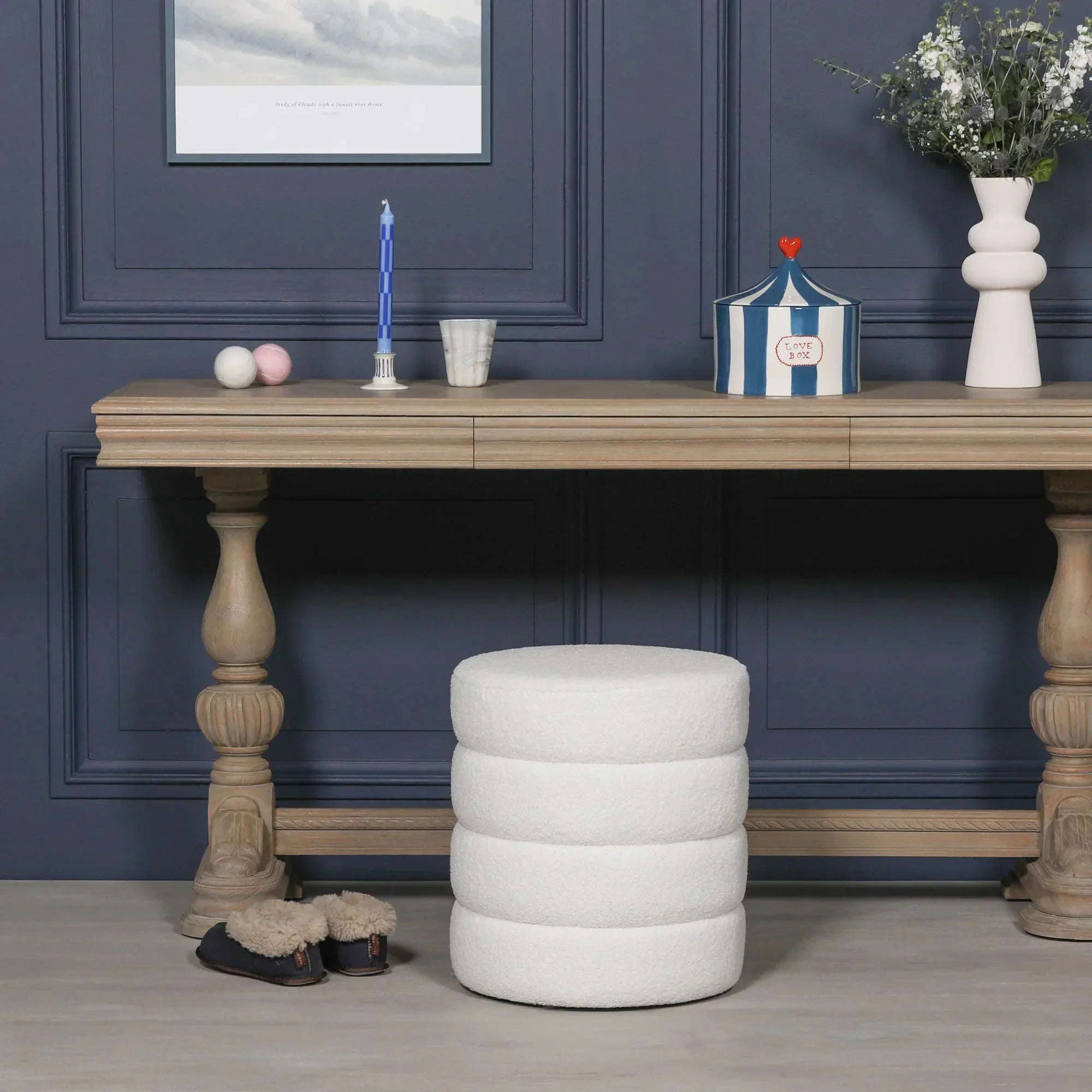 White boucle round ottoman stool in front of wooden console table with decorative items