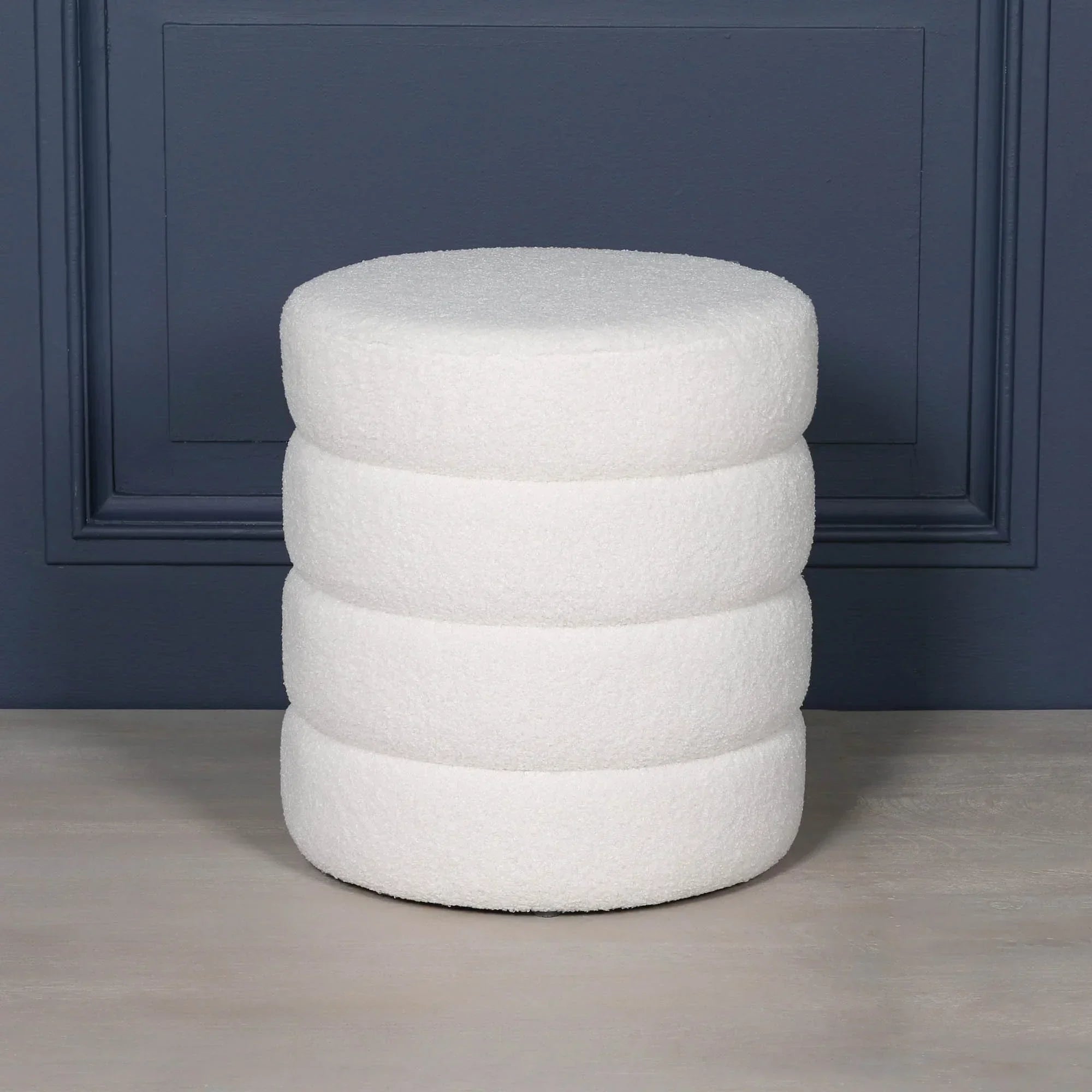 White boucle round footstool with stacked cushion design against blue wall