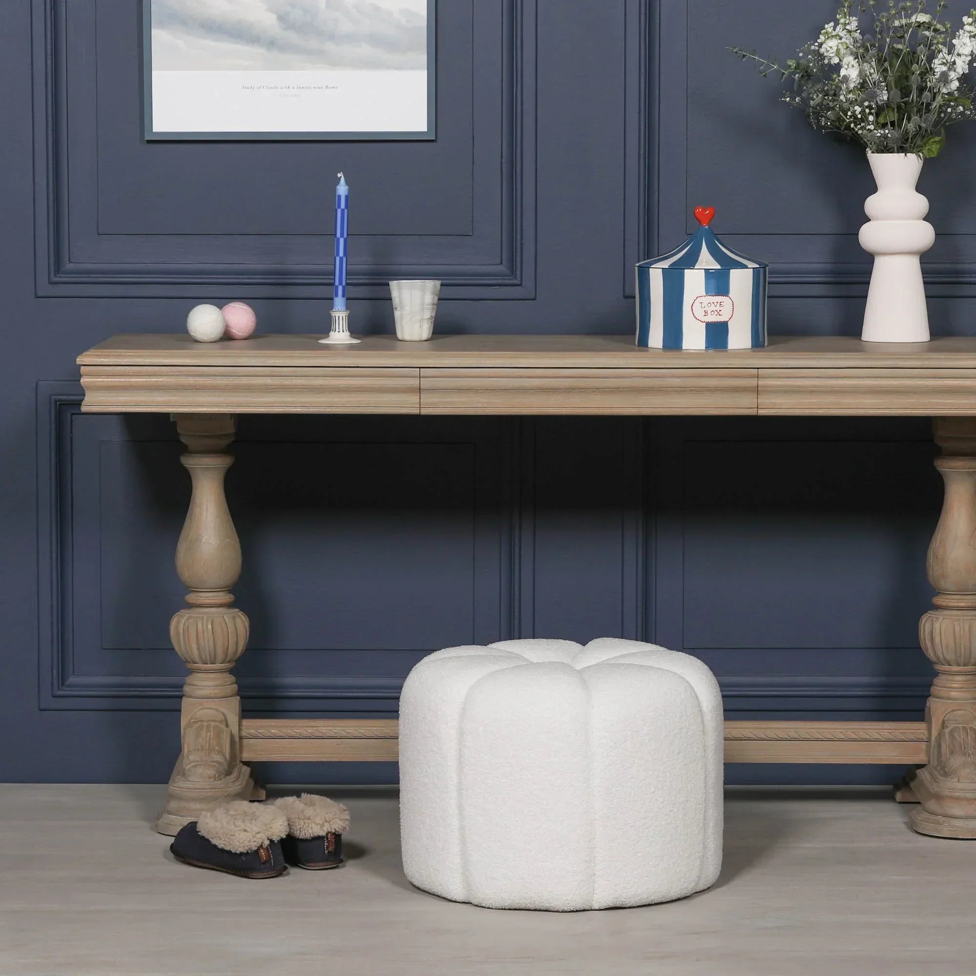 White boucle footstool with rounded design in front of wooden console table and navy wall