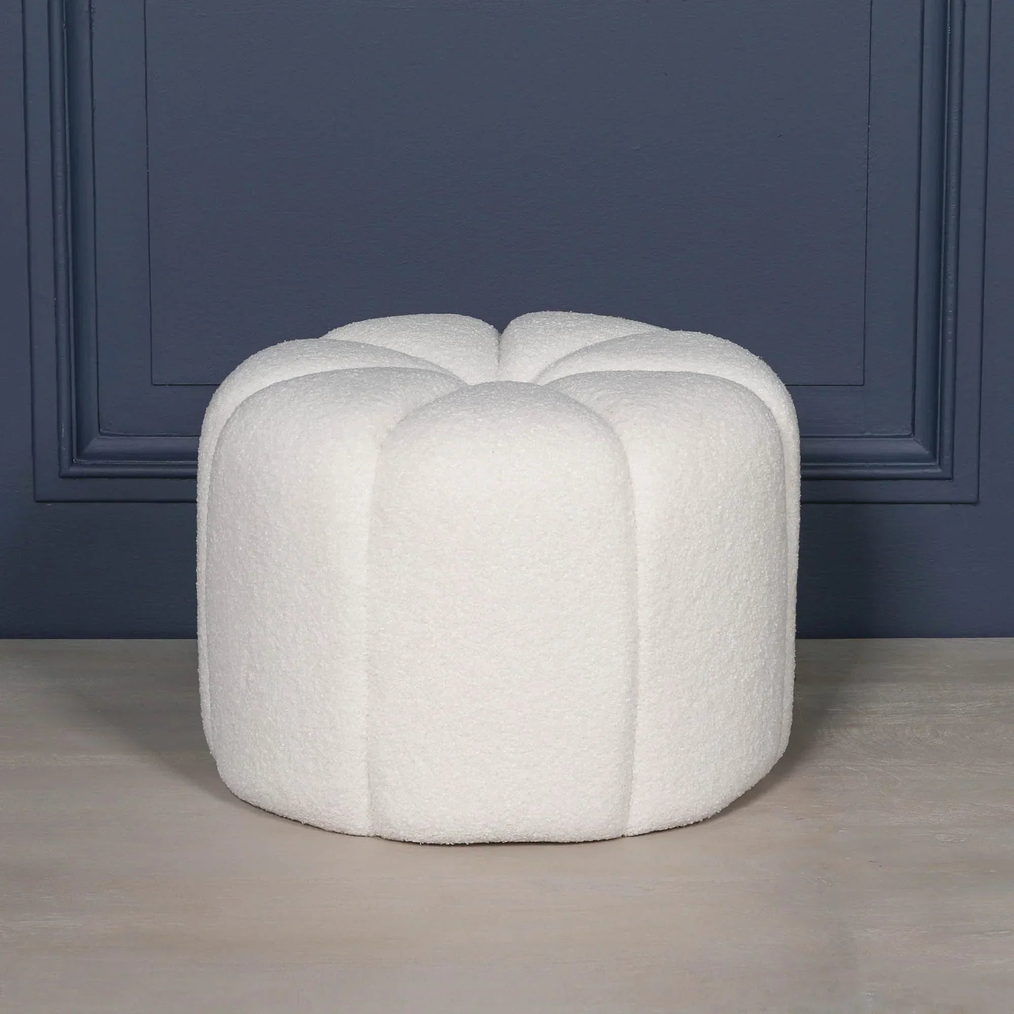 White boucle ottoman stool with scalloped edges against dark blue wall
