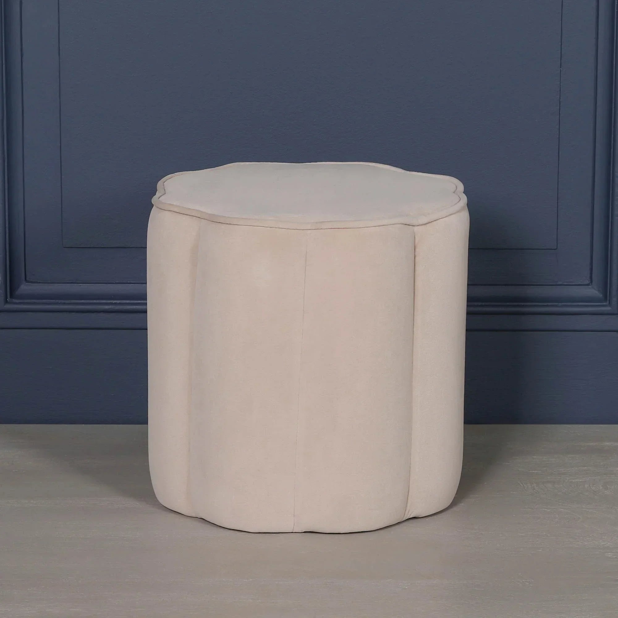 Round cream velvet ottoman with scalloped edge on grey wooden floor