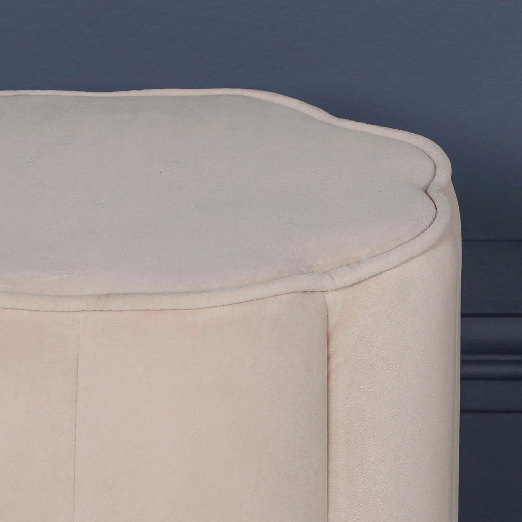 Beige velvet ottoman with scalloped top edge against blue wall