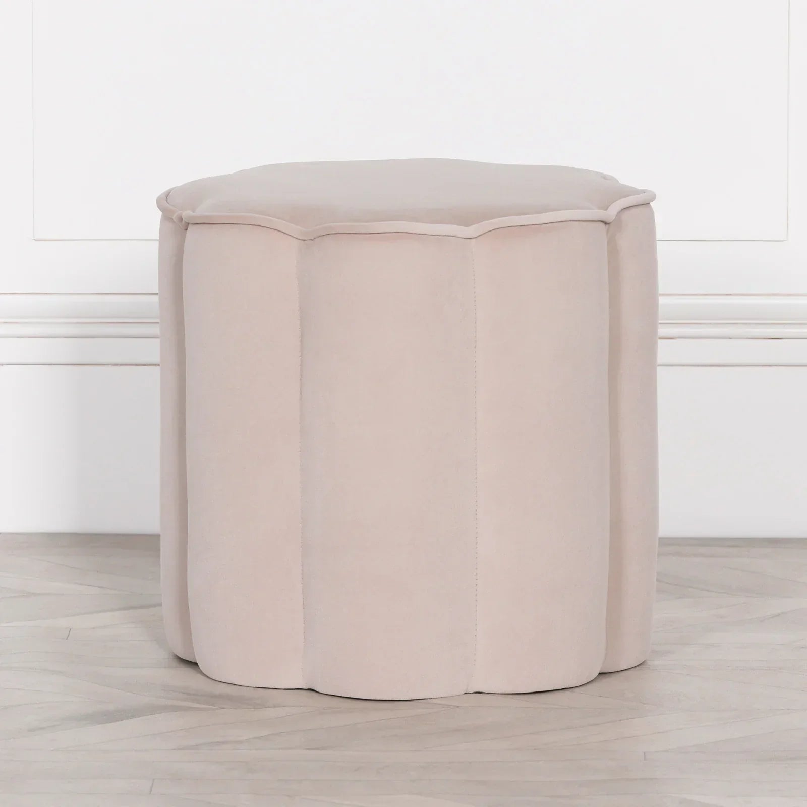 Beige velvet ottoman with scalloped sides on light wood floor