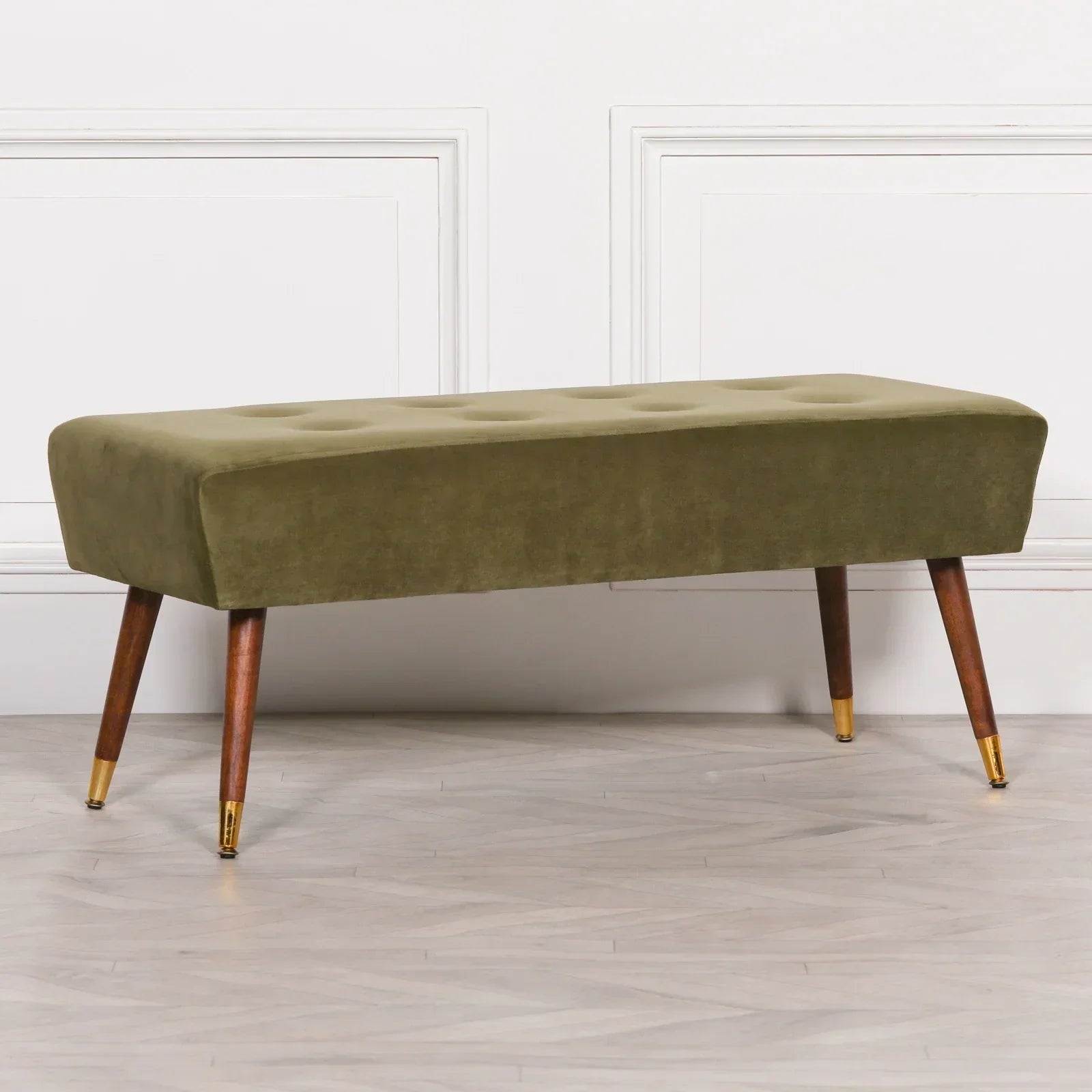 Olive green velvet bench with button-tufted seat and wooden legs with gold caps on hardwood floor