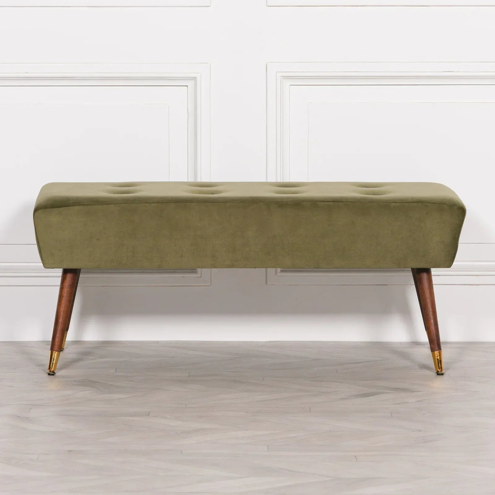 Olive green velvet bench with tufted seat and angled wooden legs on herringbone floor