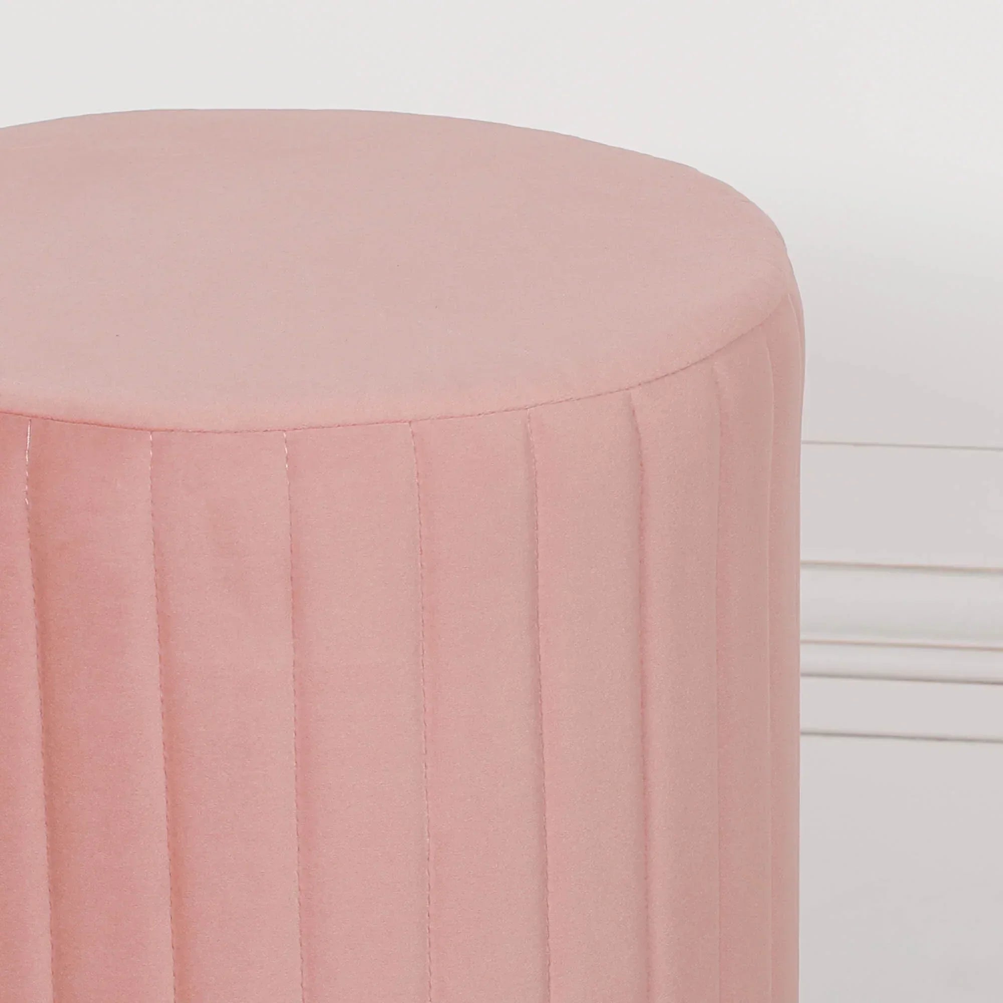 Pink velvet round ottoman with vertical stitched detail against a white background