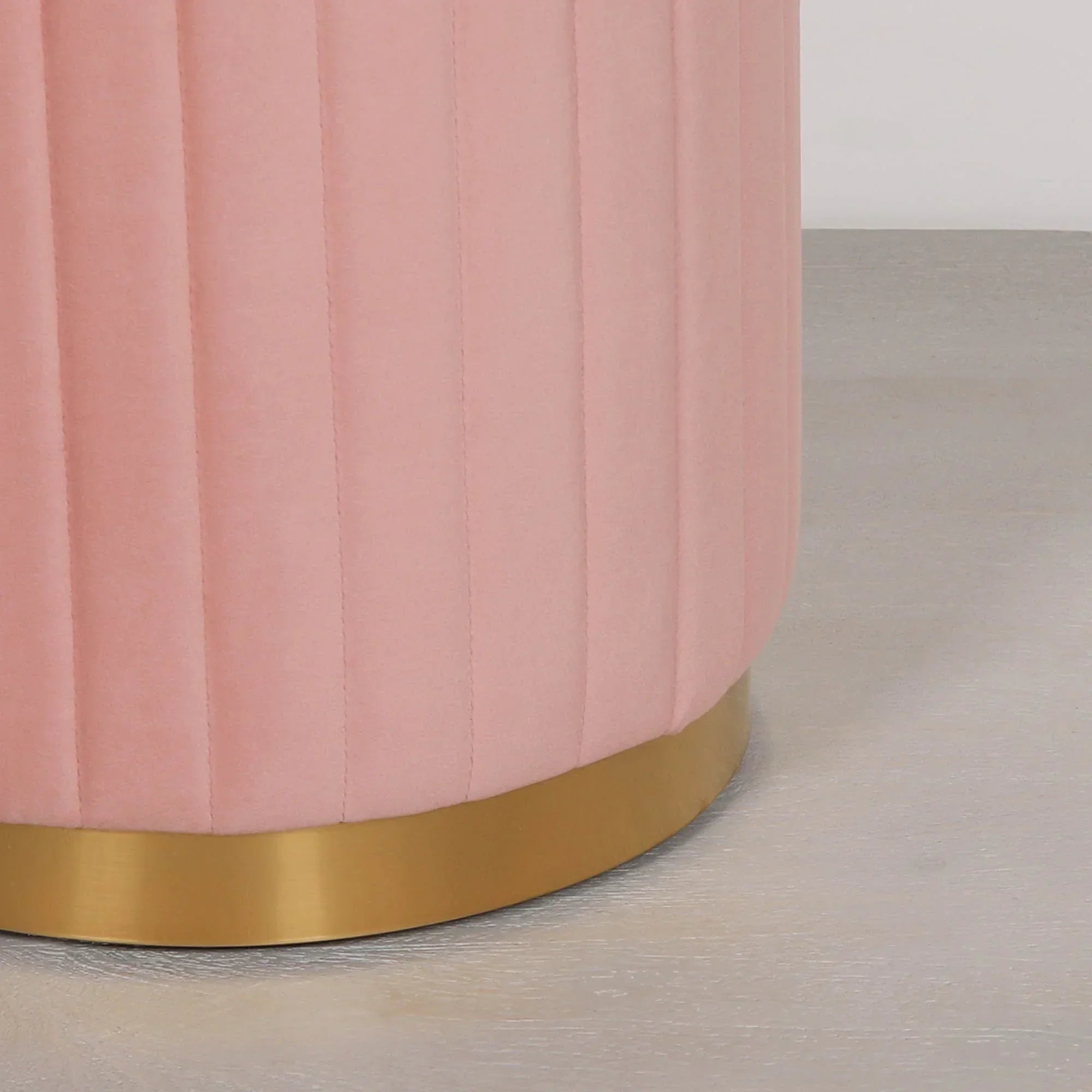 Close-up of pink velvet ottoman with gold metal base on light wood floor