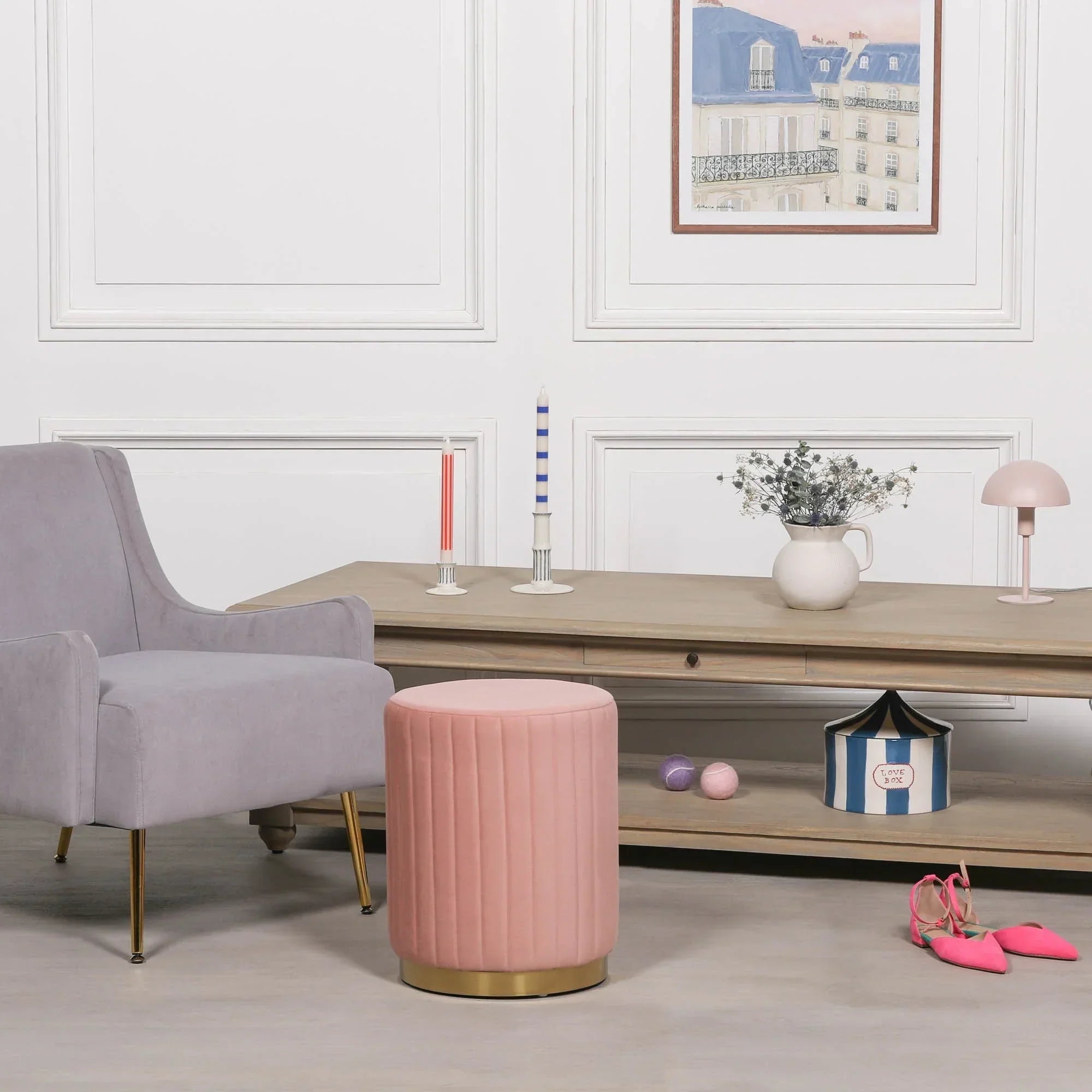 Pink velvet footstool with gold base in living room beside grey armchair and wooden console table