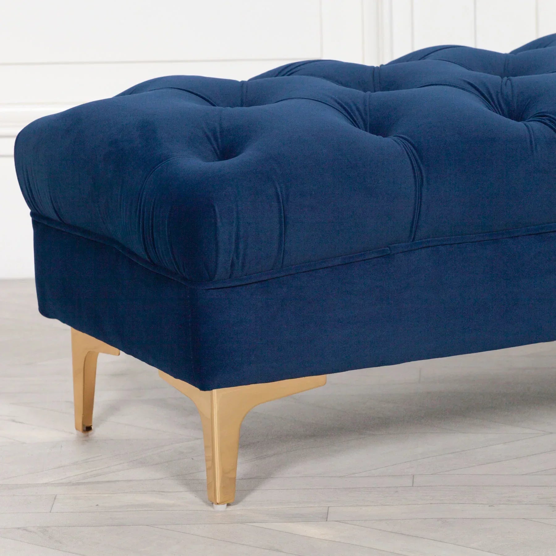 Navy velvet ottoman with button tufting and gold legs on light wood floor