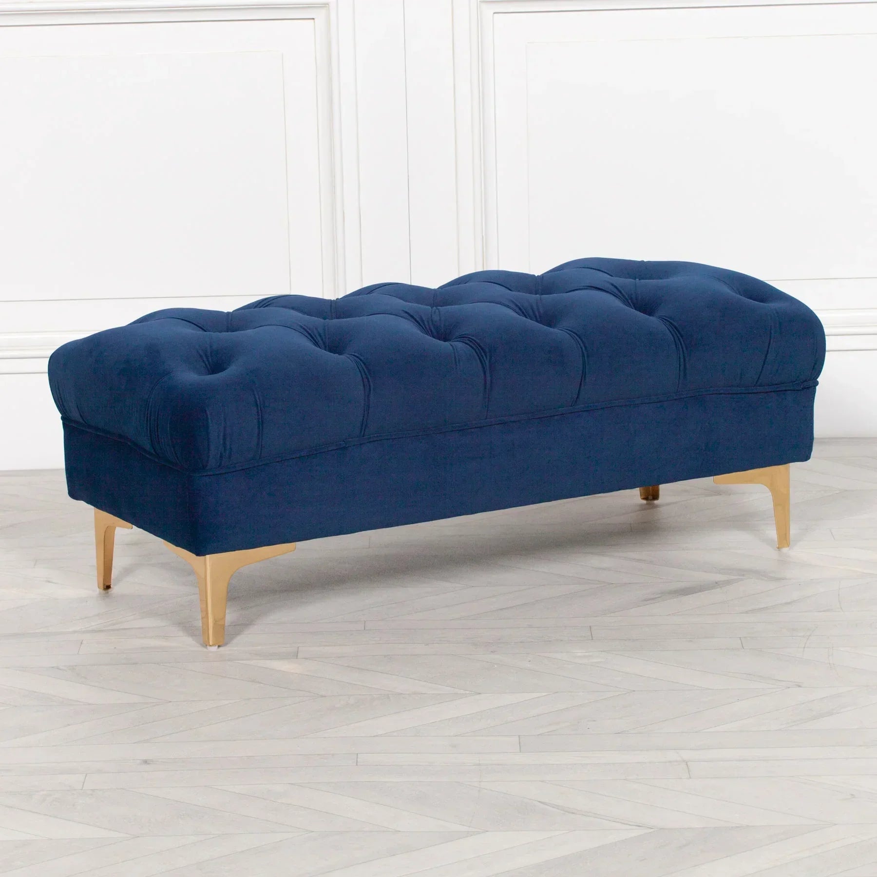 Navy blue upholstered bench with button tufting and gold legs on light wood floor
