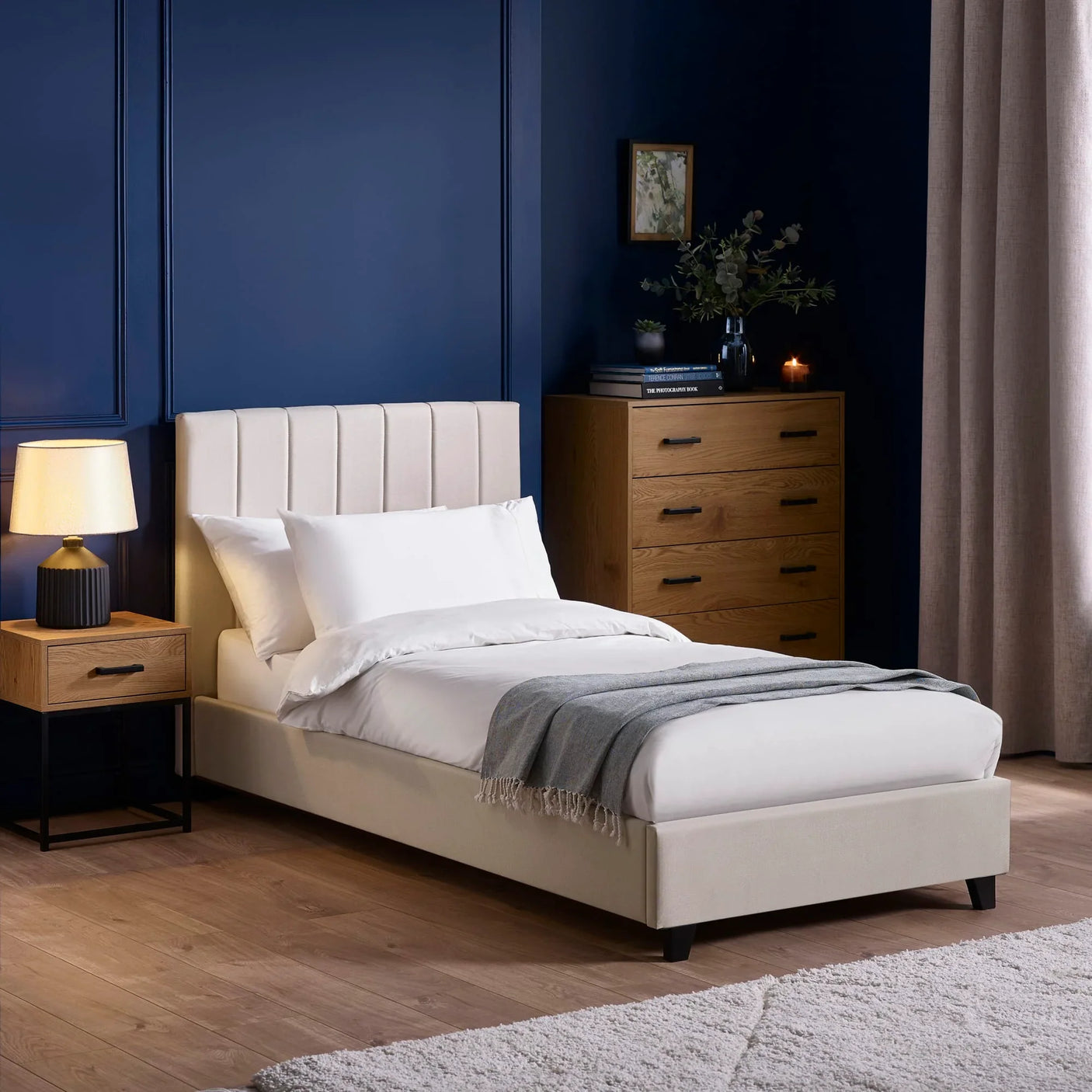 Beige single bed with upholstered headboard in modern bedroom, oak nightstand and drawers