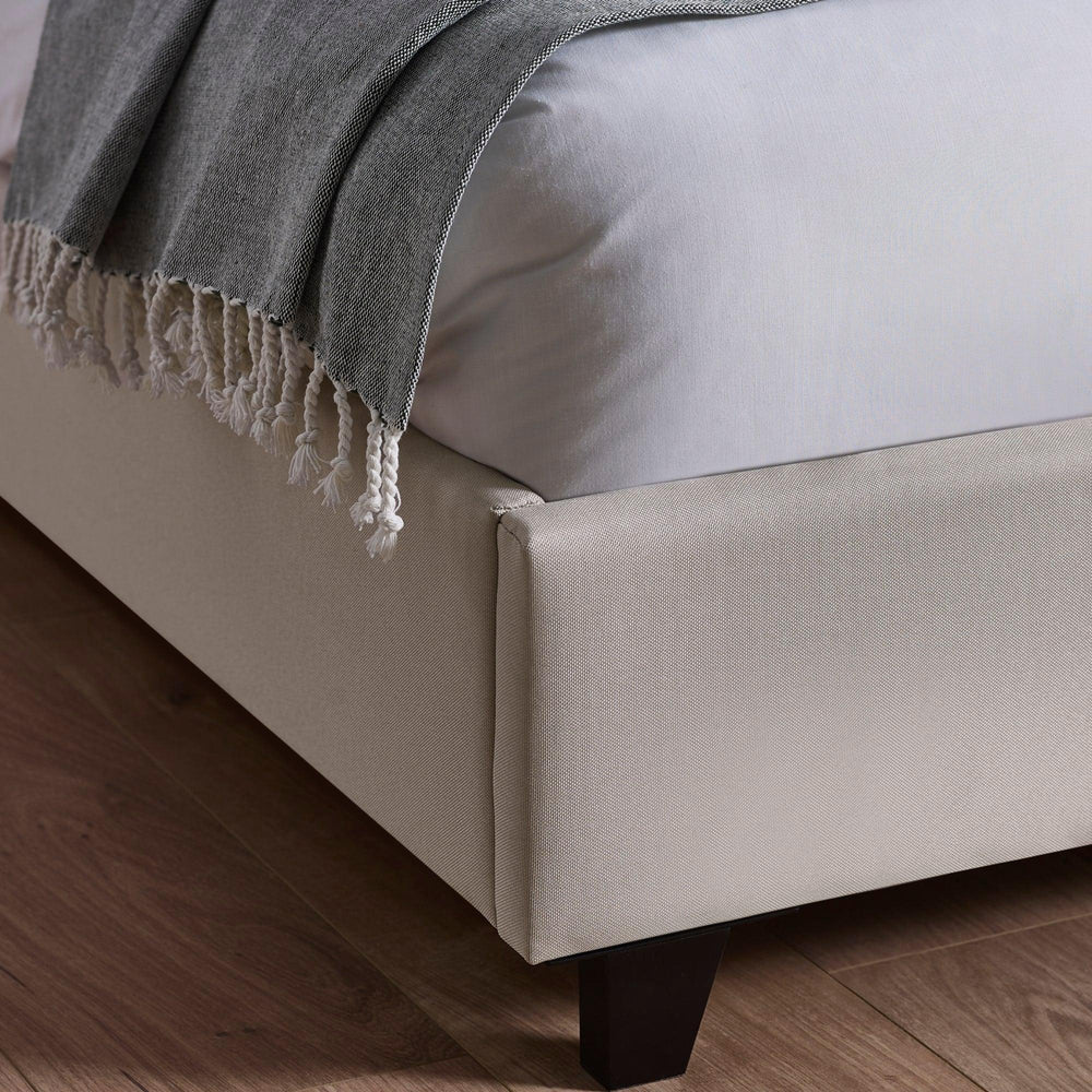 Beige fabric bed frame corner with dark wooden leg on wooden floor