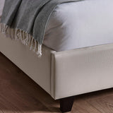 Beige fabric bed frame corner with dark wooden leg on wooden floor