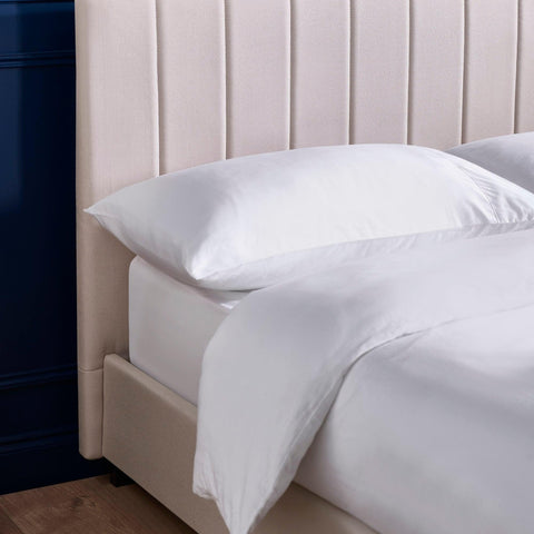 Beige upholstered bed frame with vertical panel headboard and white bedding