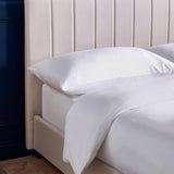 Beige upholstered bed frame with vertical panel headboard and white bedding