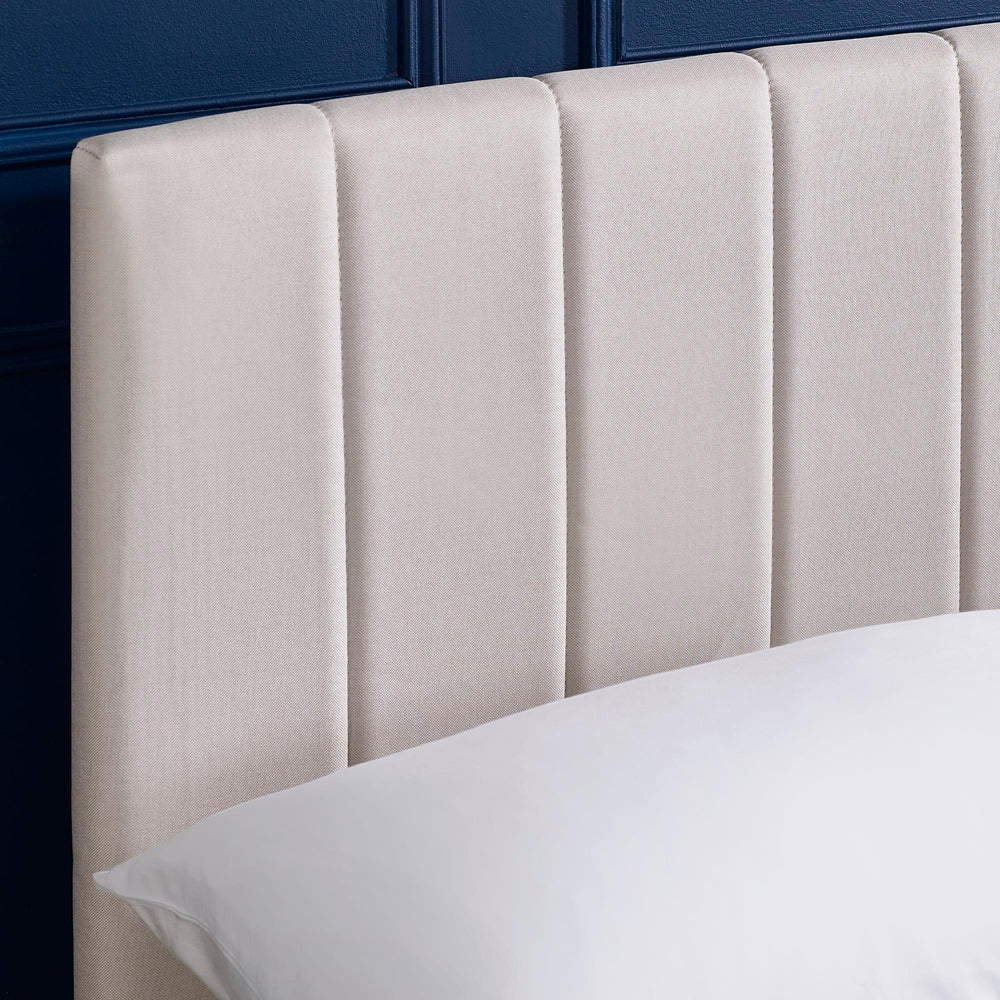 Beige upholstered headboard with vertical panel design against navy wall