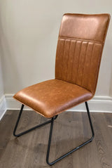 Cognac leather dining chair with metal legs and stitched backrest on wood floor